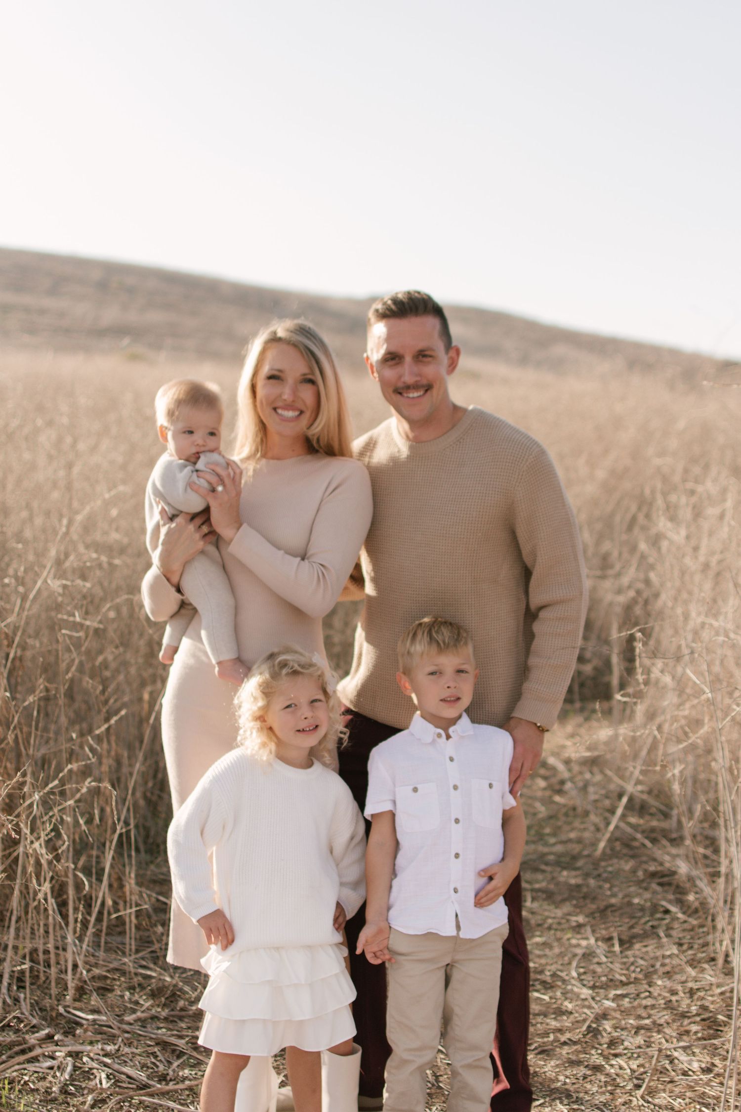Happy family of five posing in a golden field of tall dry grass on a sunny day.