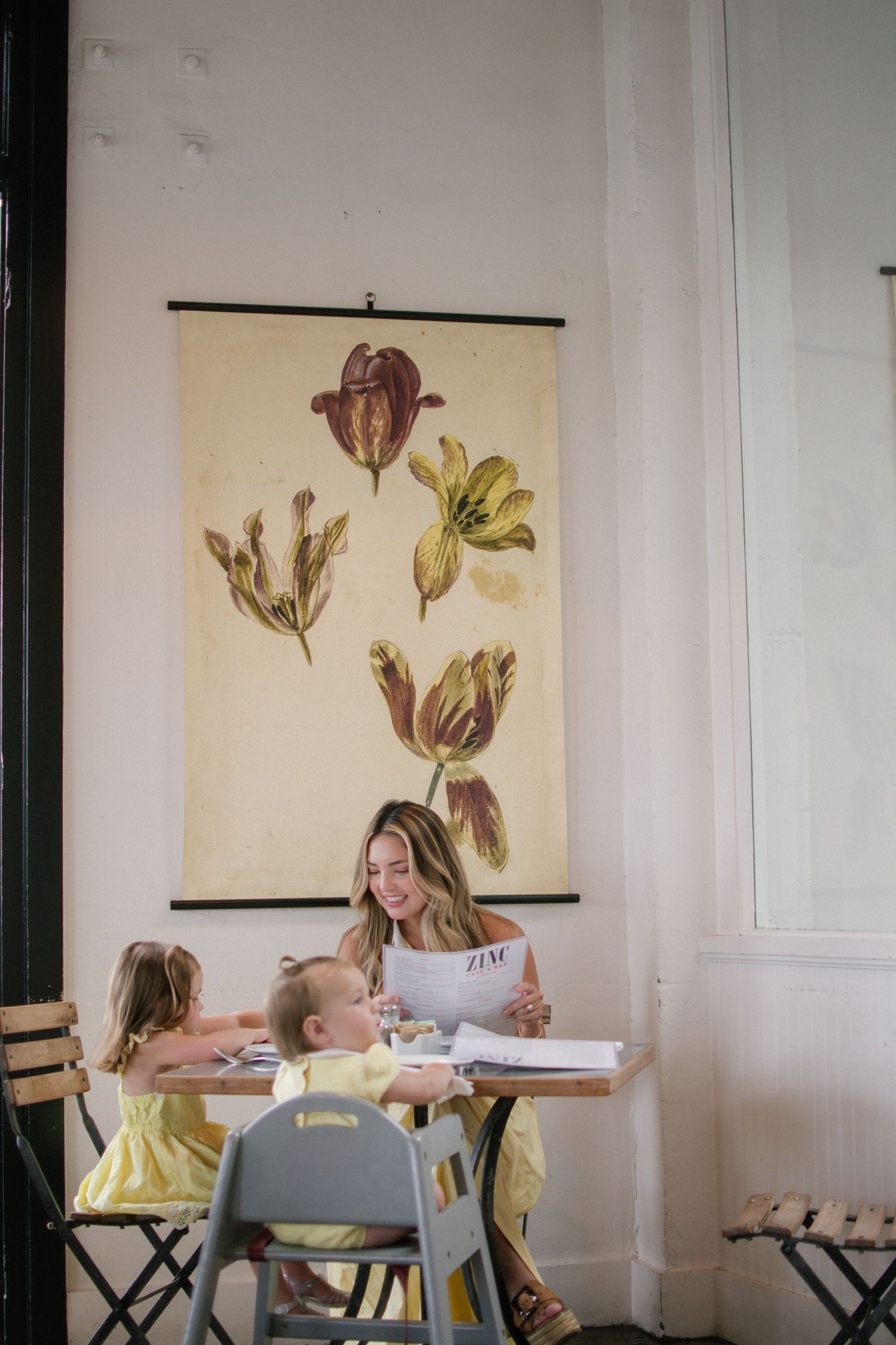 Woman reading a magazine with two young children at a cafe table.