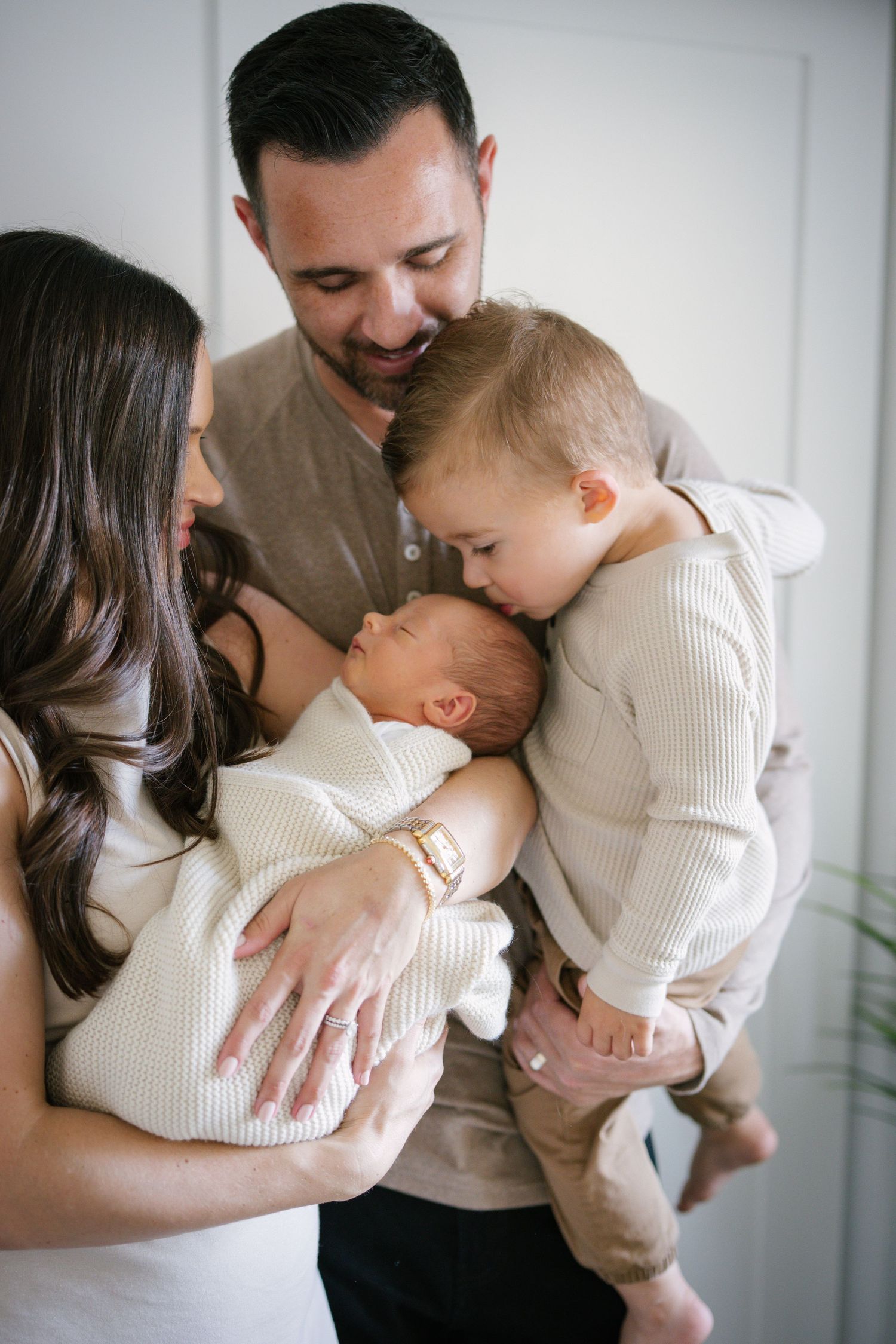 Happy family of four admiring their newborn baby together indoors.