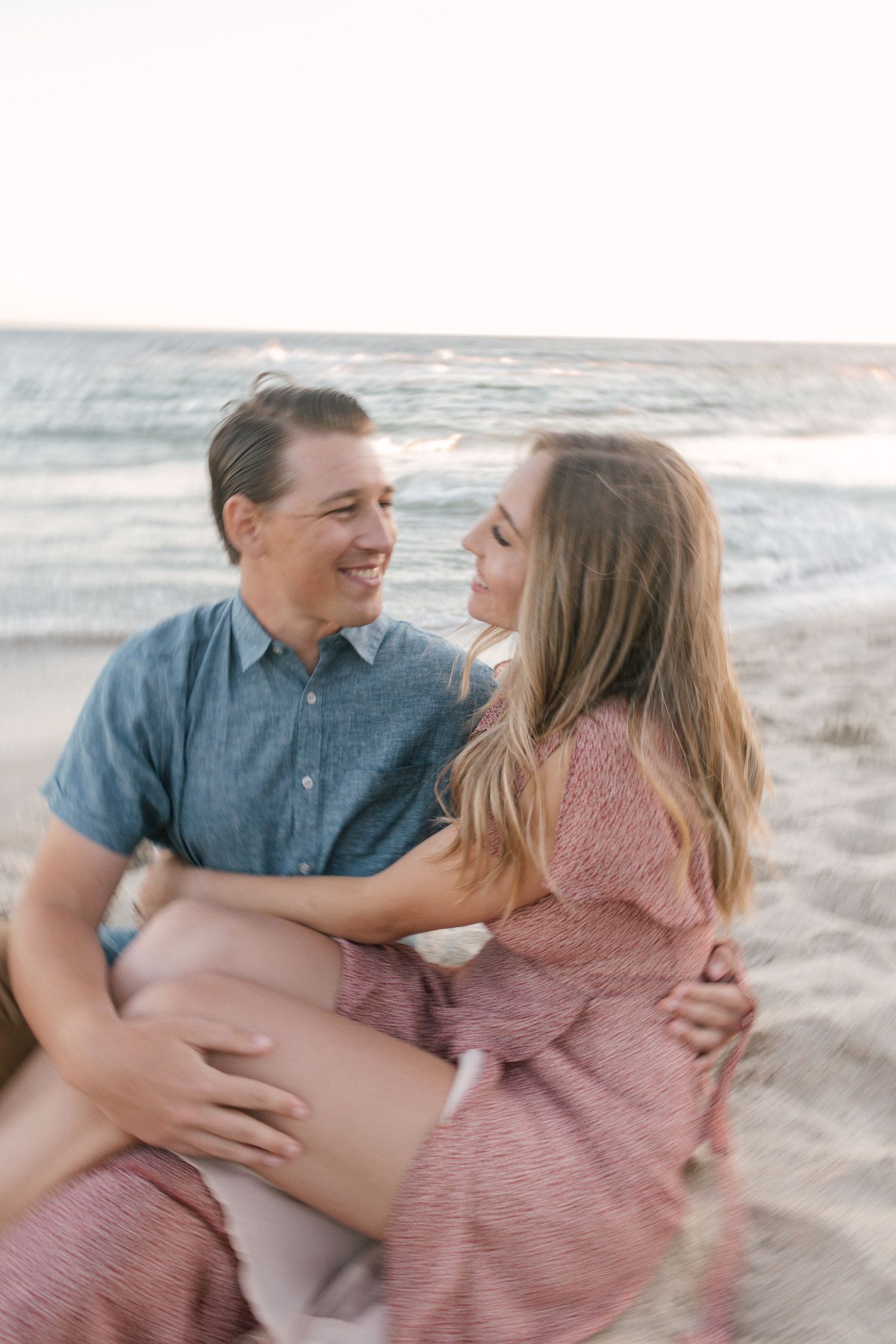 Couple sitting together on sandy beach smiling at each other at sunset.
