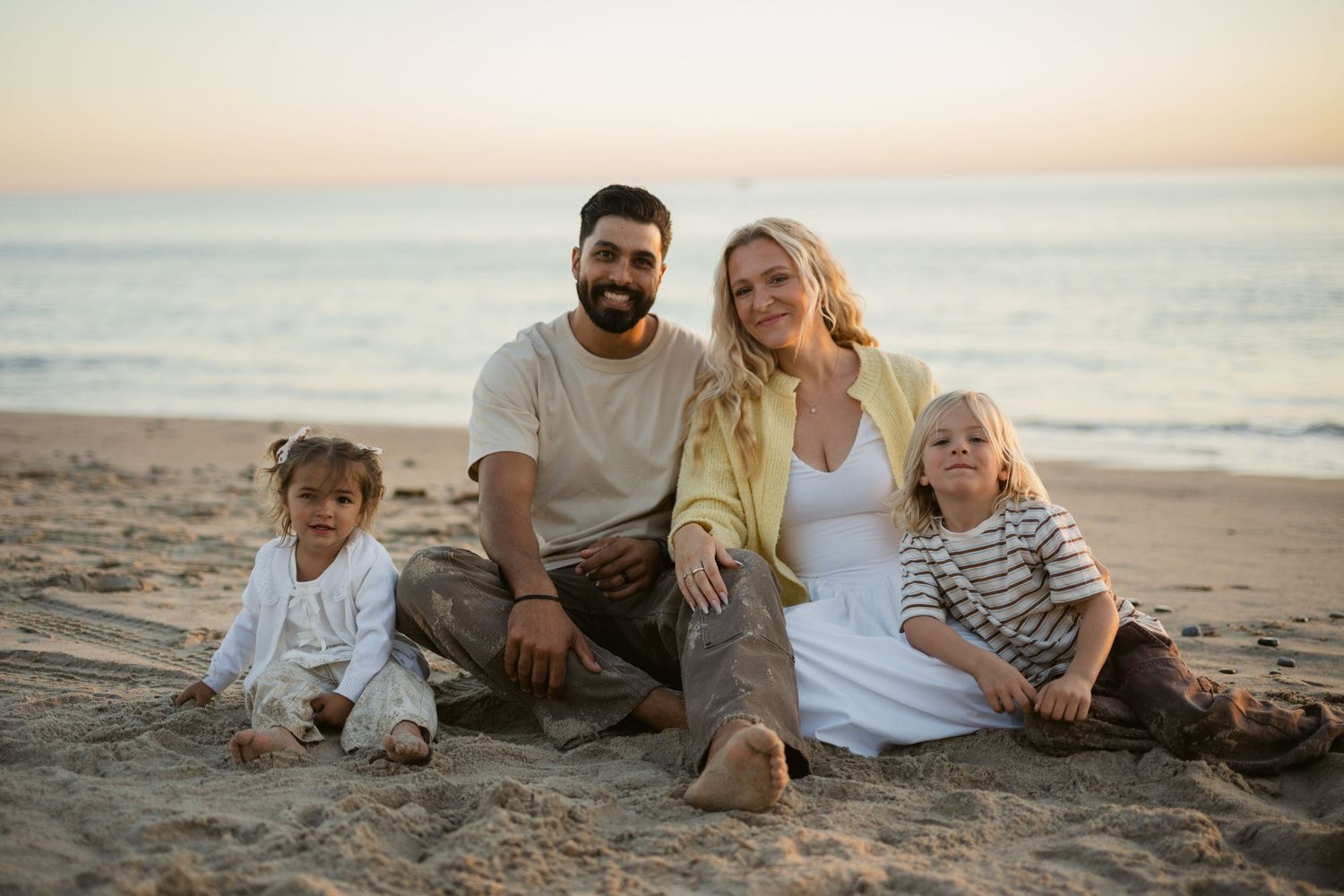 Happy family of four sitting together on a sandy beach during a warm sunset evening.