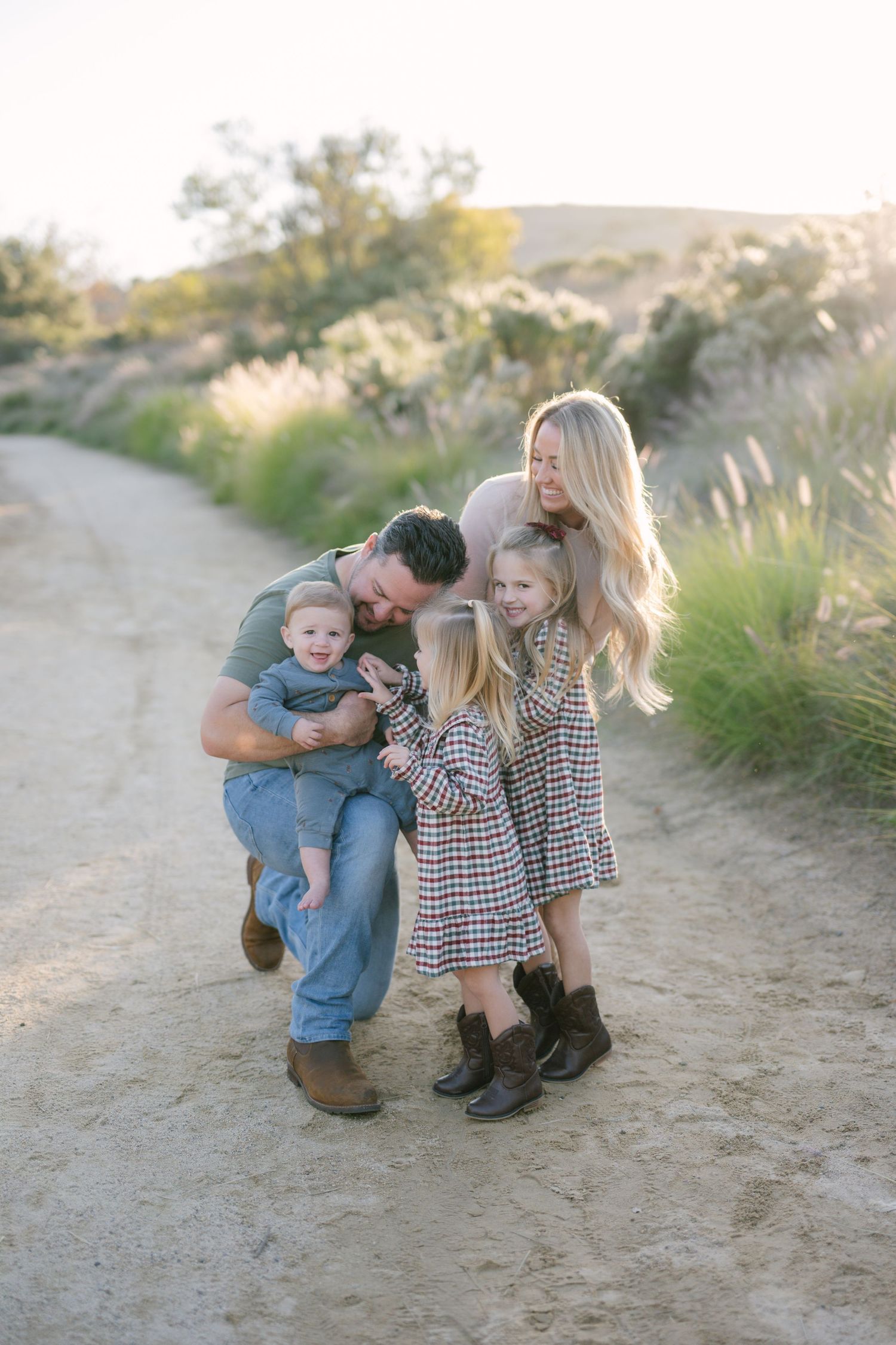Family of four sharing a joyful moment on a sandy path with golden grasses at sunset.