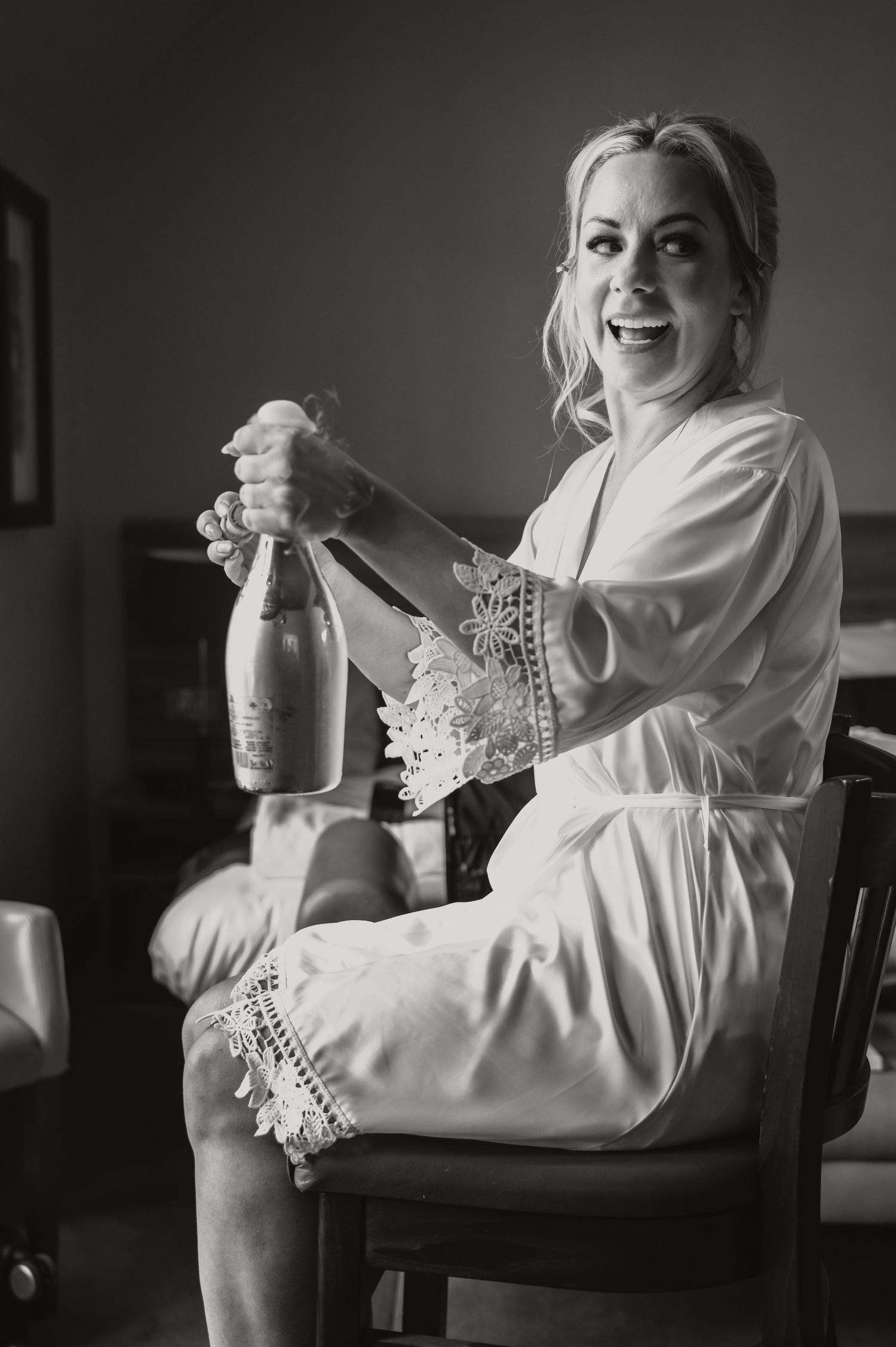Wedding preparation scene with person in white robe holding champagne bottle.