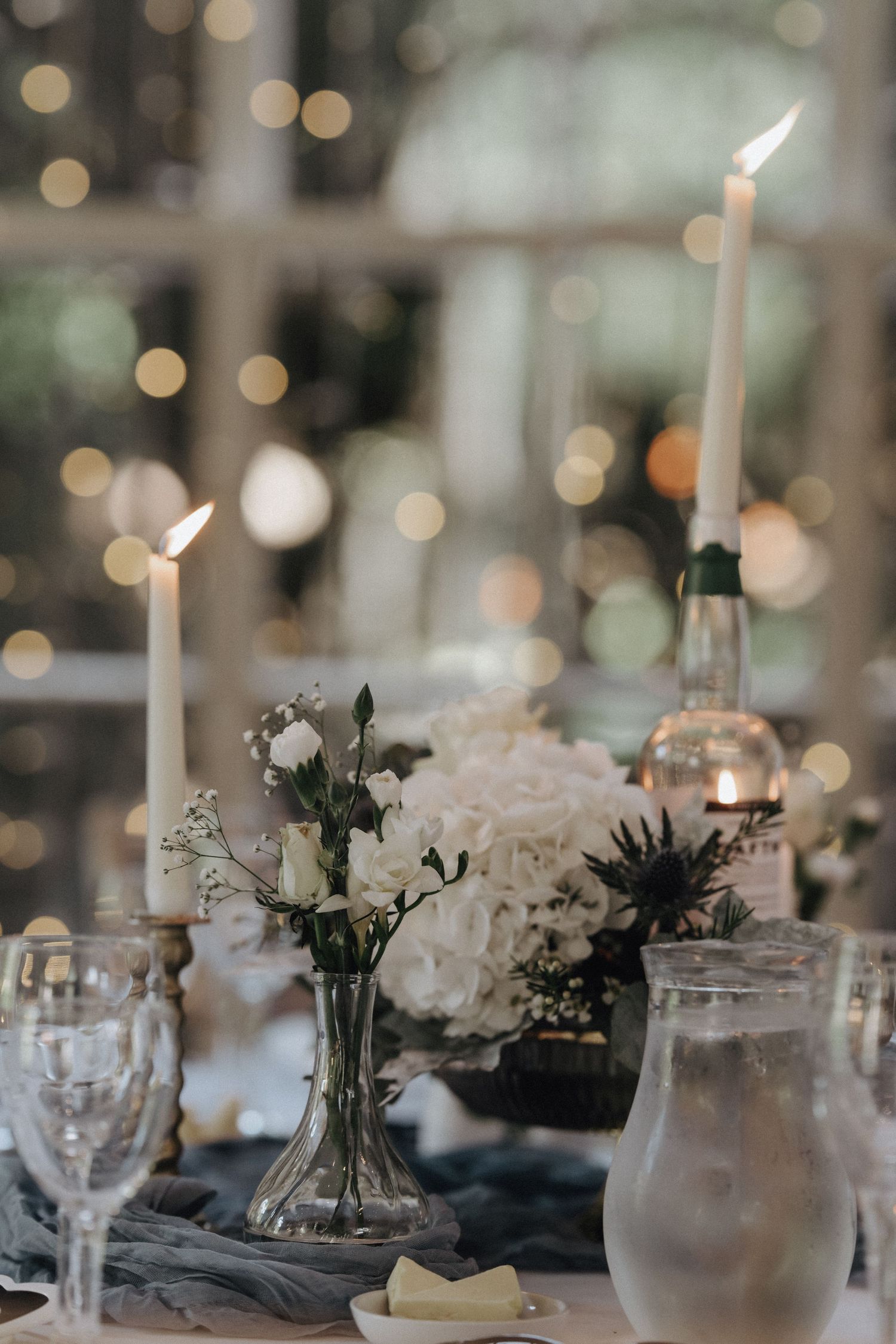 Elegant wedding reception table with white floral centerpieces and glowing candles.