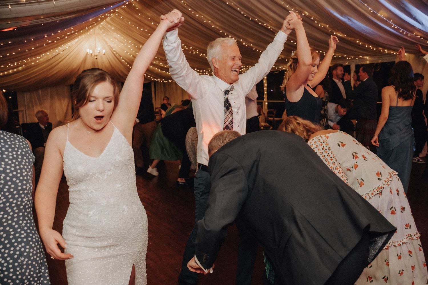 Guests celebrating and dancing energetically at a wedding reception under string lights.