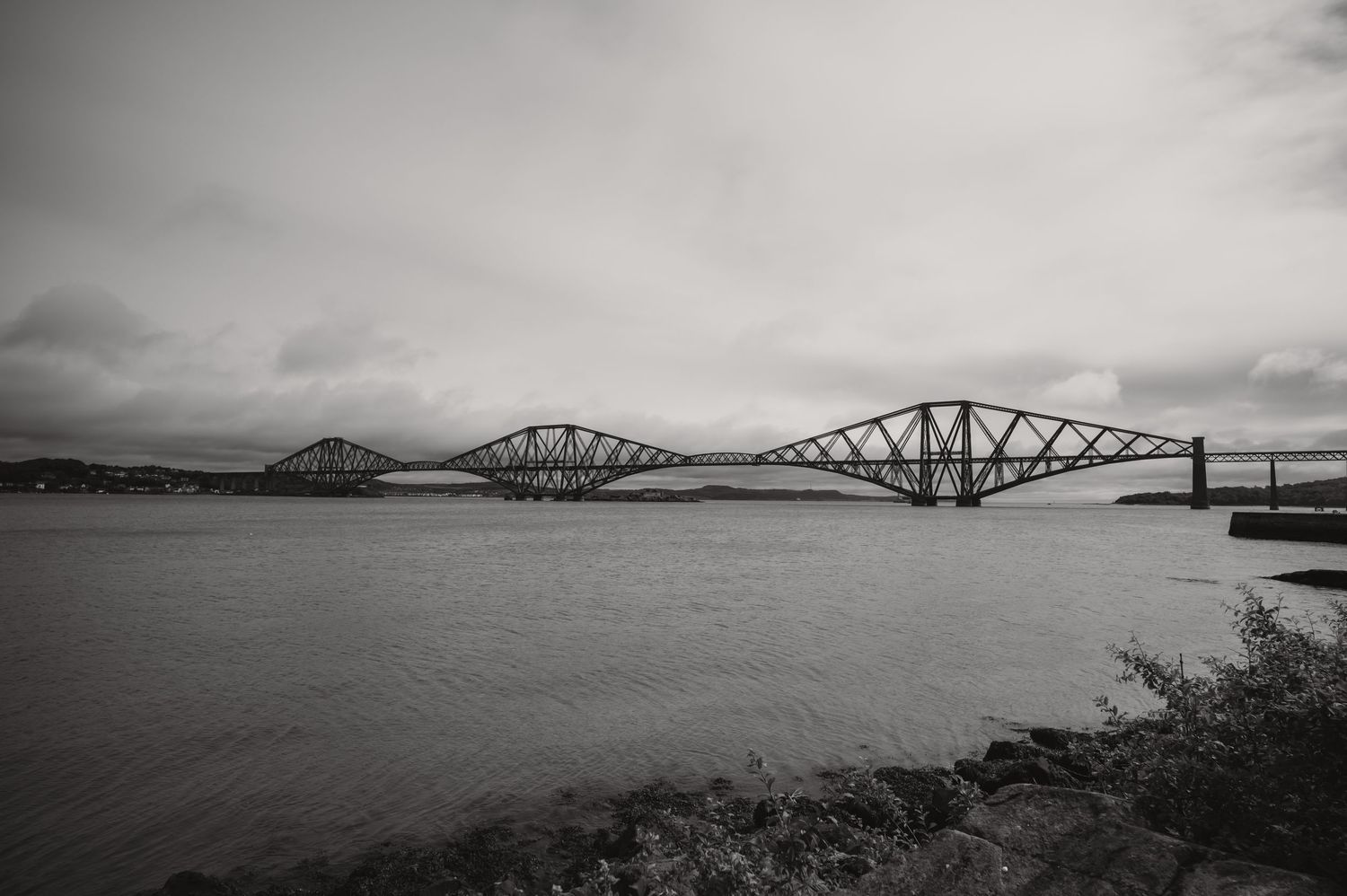Black and white photograph of the iconic Forth Bridge in Scotland spanning across calm waters.