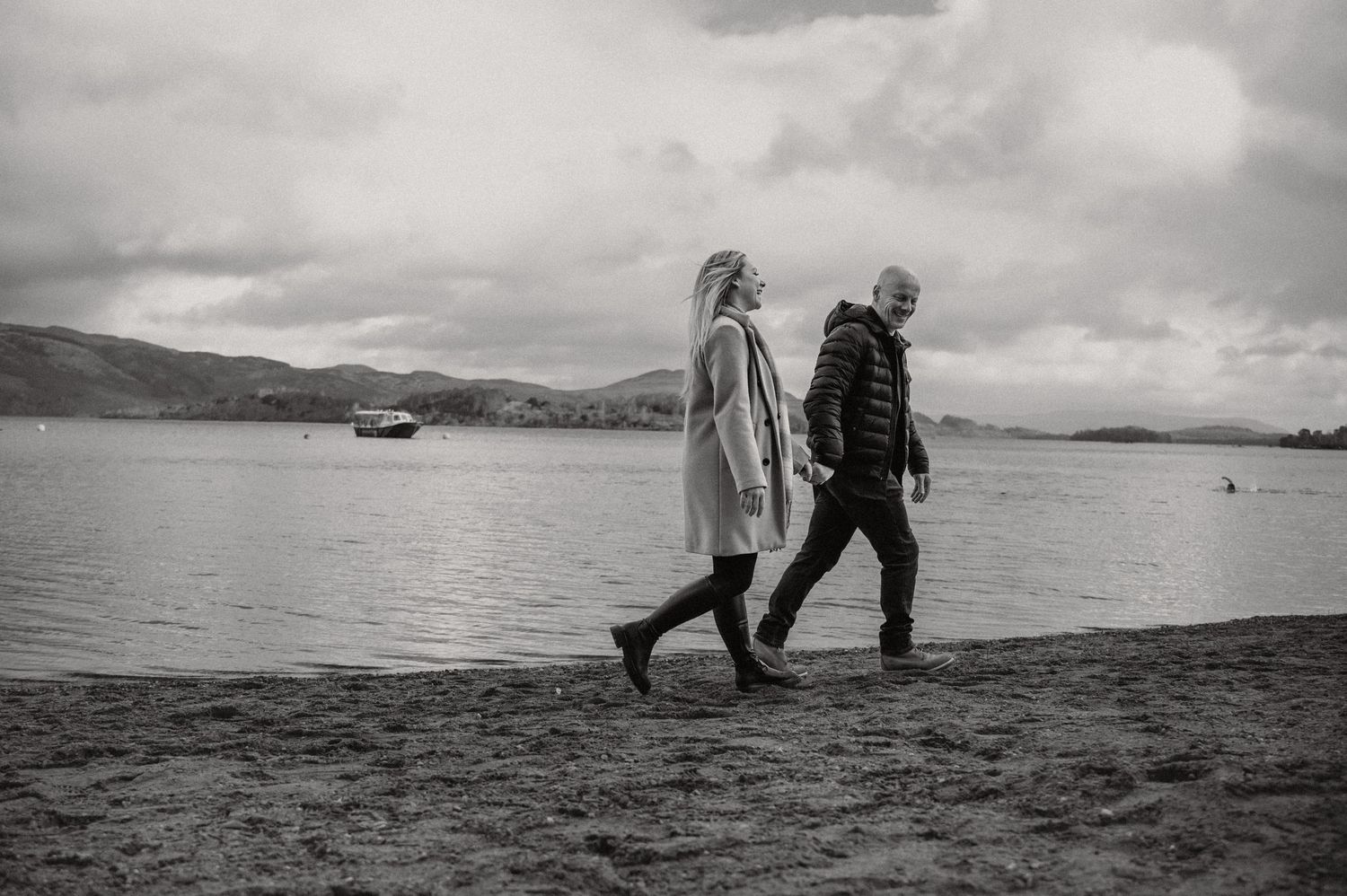A black and white photo of a couple walking along a misty lakeshore.
