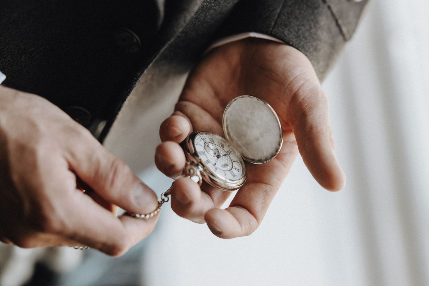 Close-up of hands holding antique pocket watch or timepiece against white background.