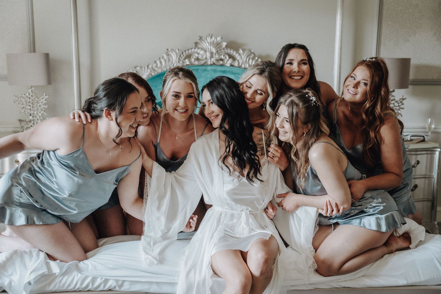 Bridal party in robes and silk pajamas sharing joyful moment together on bed.