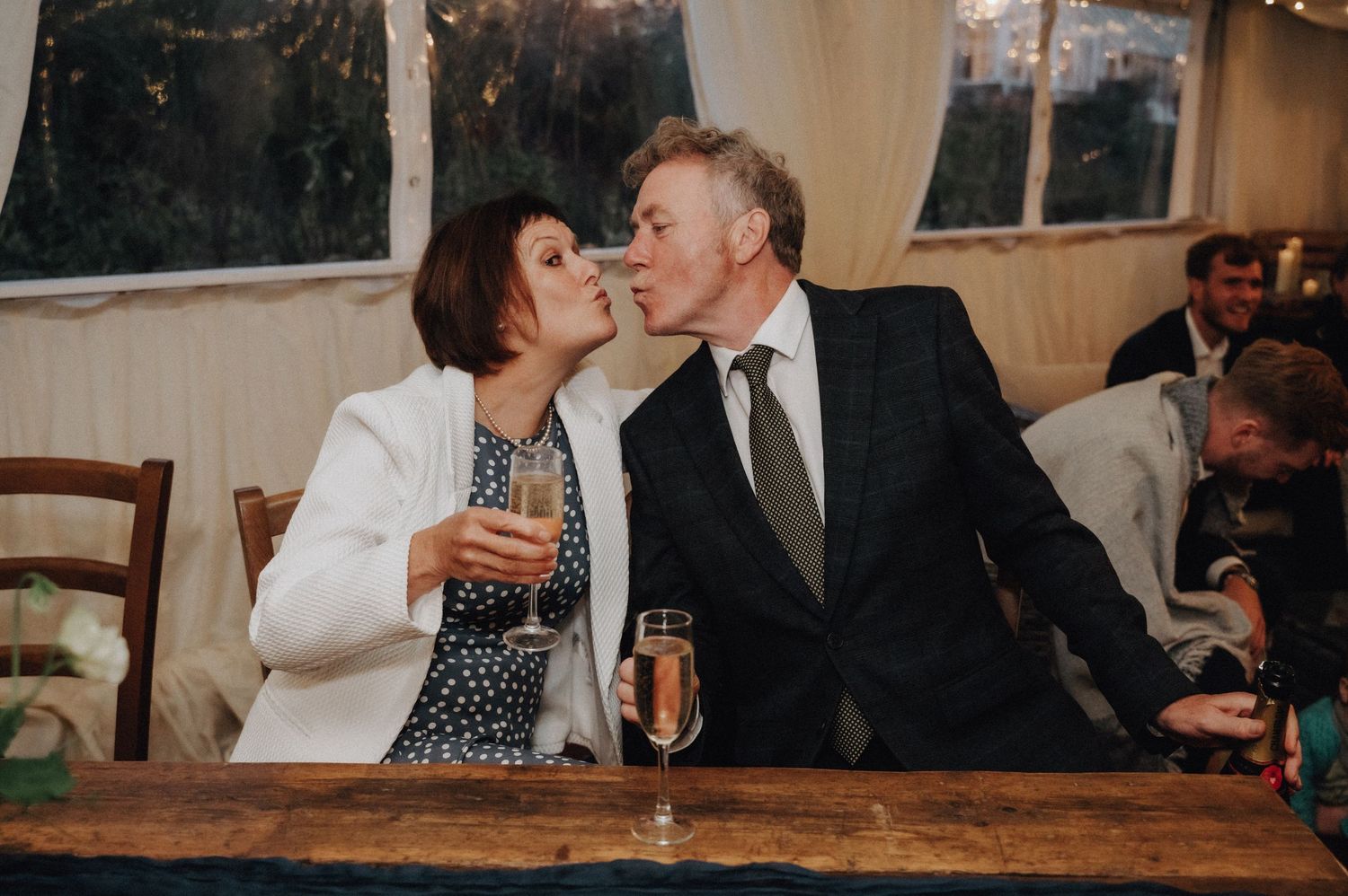 Couple shares intimate moment while toasting with champagne at reception table.