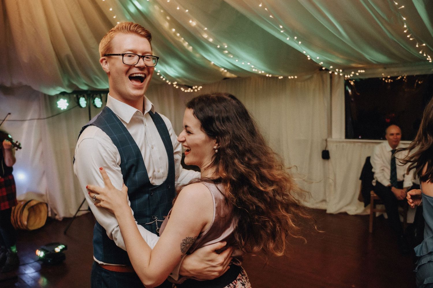 Joyful couple dancing together at wedding reception under twinkling lights.
