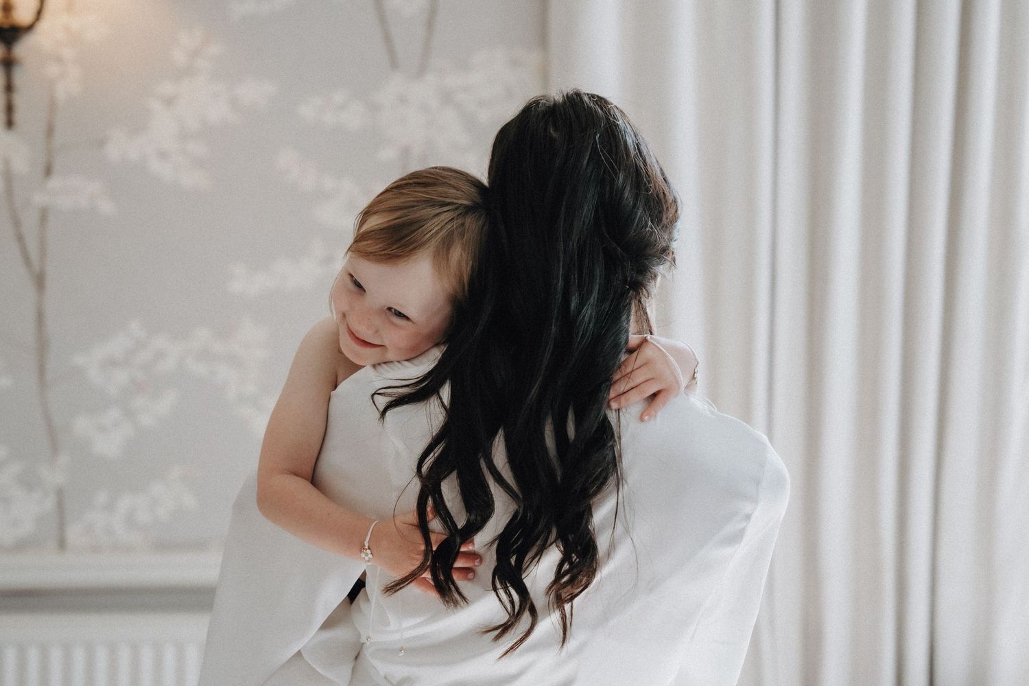 A touching moment between two people in white captured near a bright window.