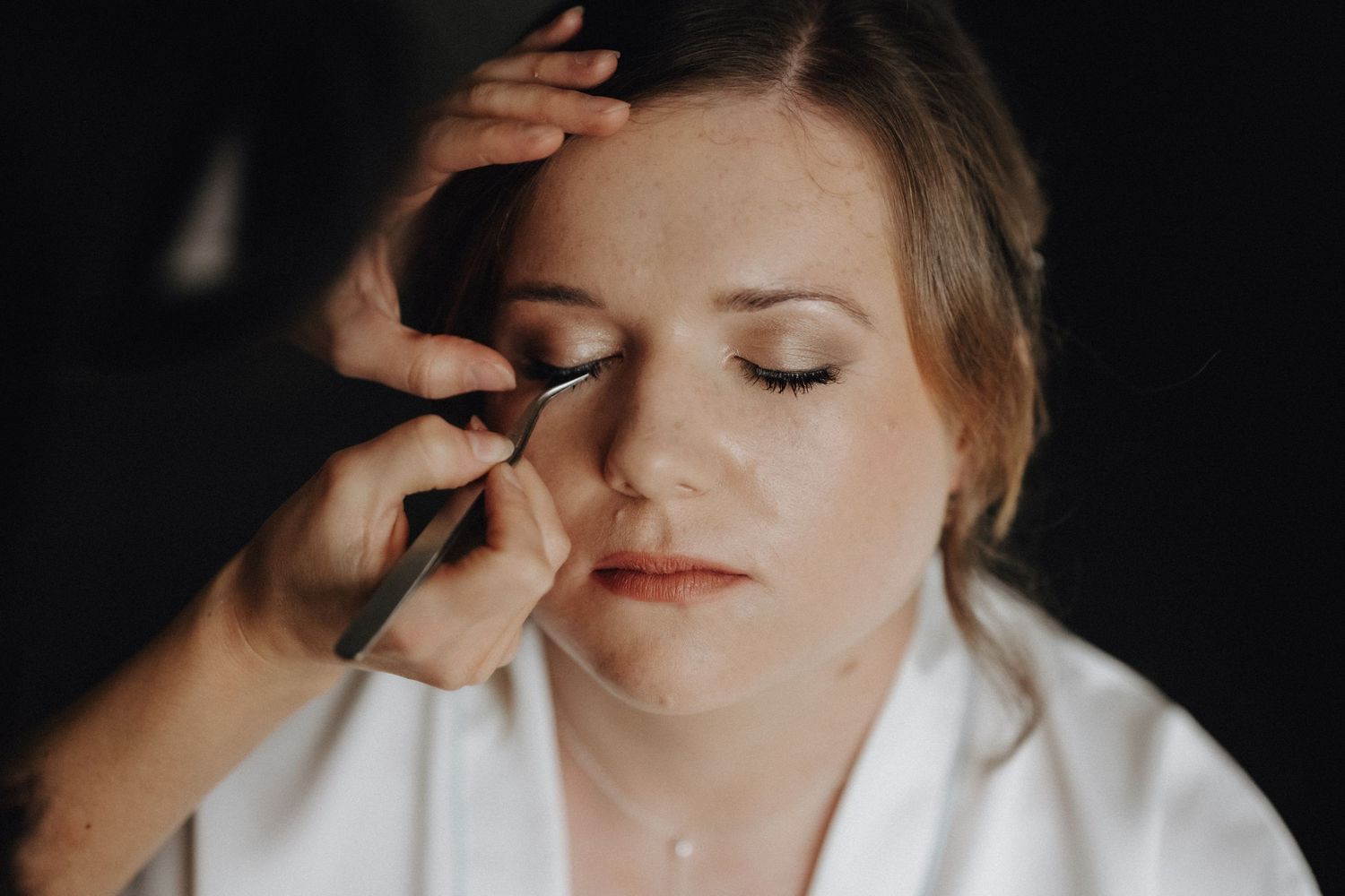 Close-up shot of makeup being applied to closed eyes in dramatic lighting.