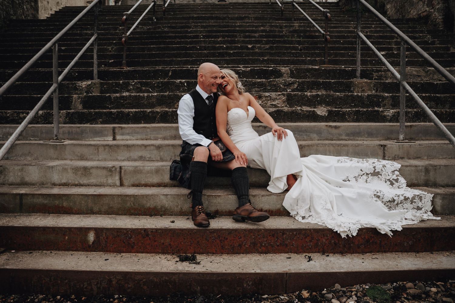 Black and white photo of people sitting on concrete steps with a wedding dress flowing down.
