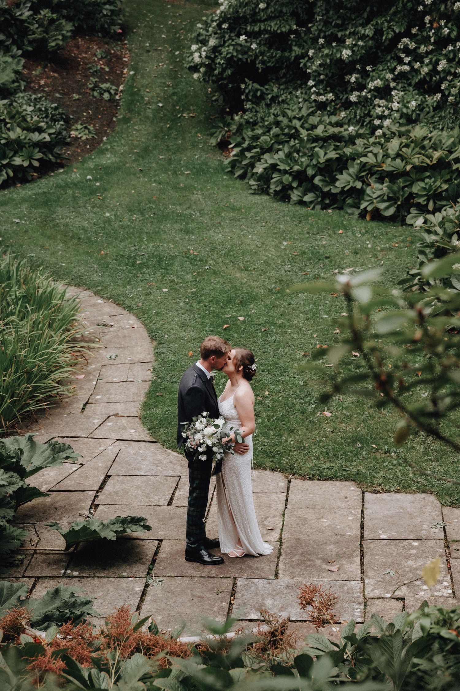 Couple shares intimate moment on stone garden steps surrounded by lush greenery.