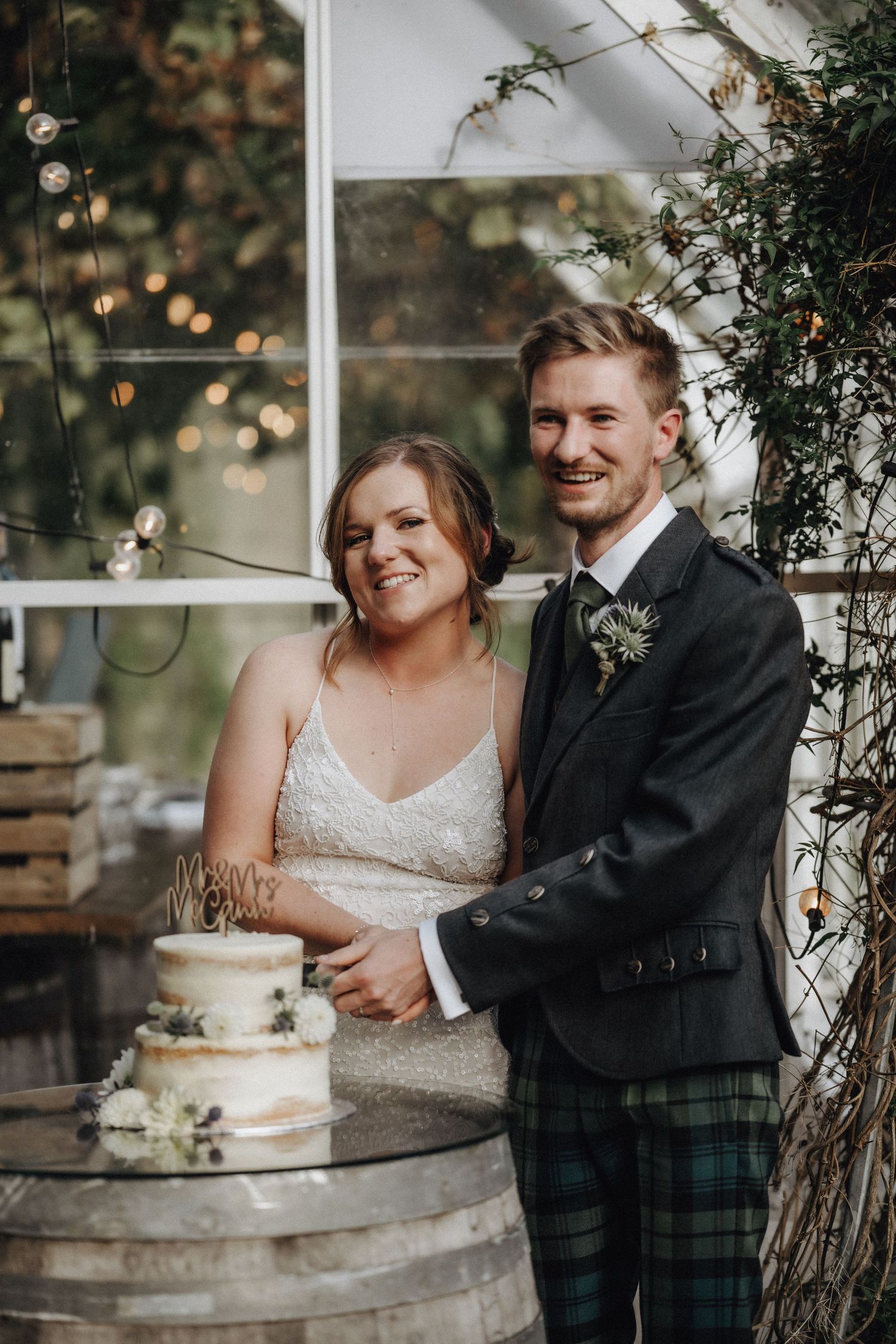 Newlyweds share a joyful moment while cutting their wedding cake on rustic barrel display.