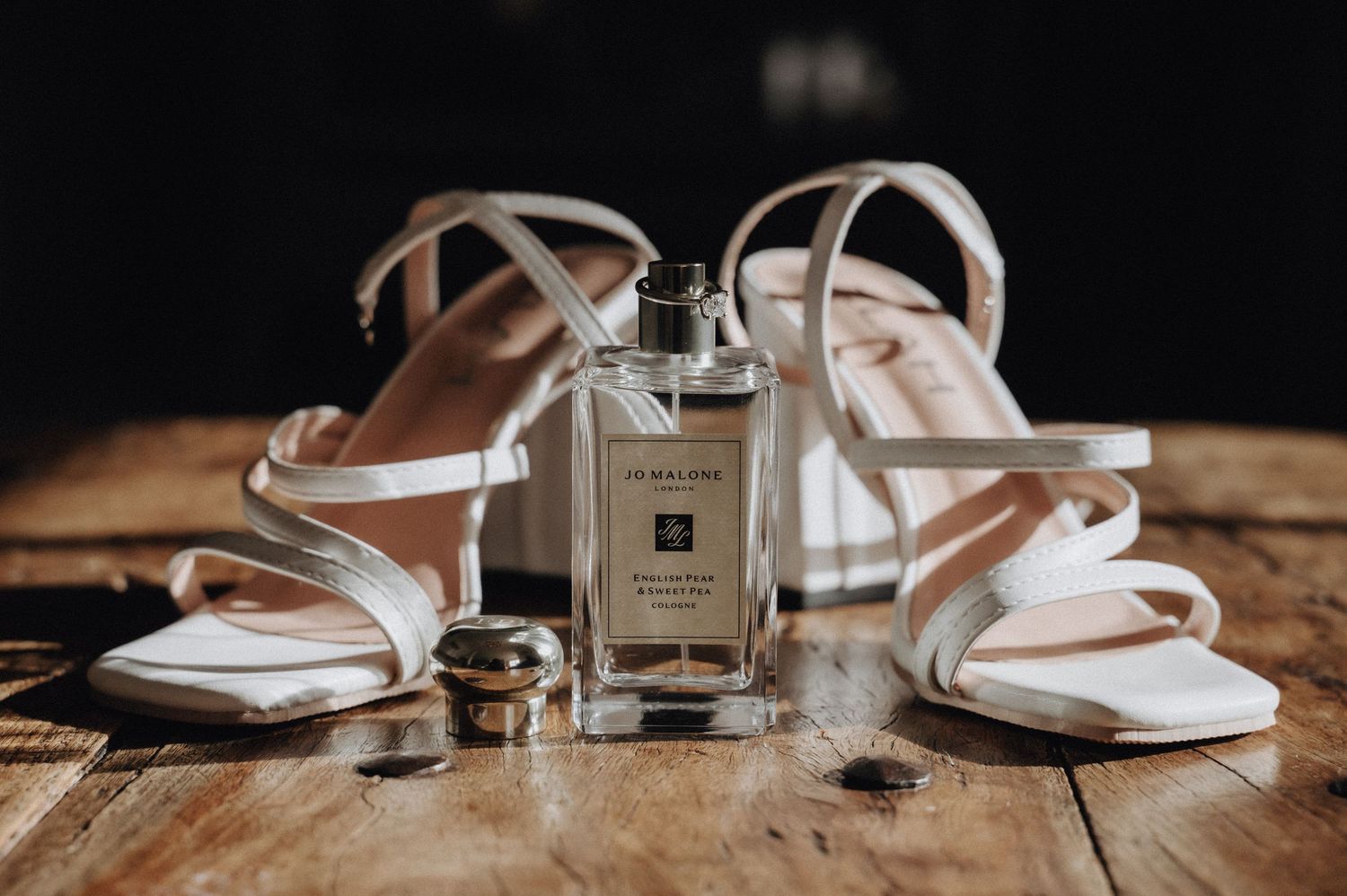 White bridal sandals and perfume bottle arranged on rustic wooden surface.
