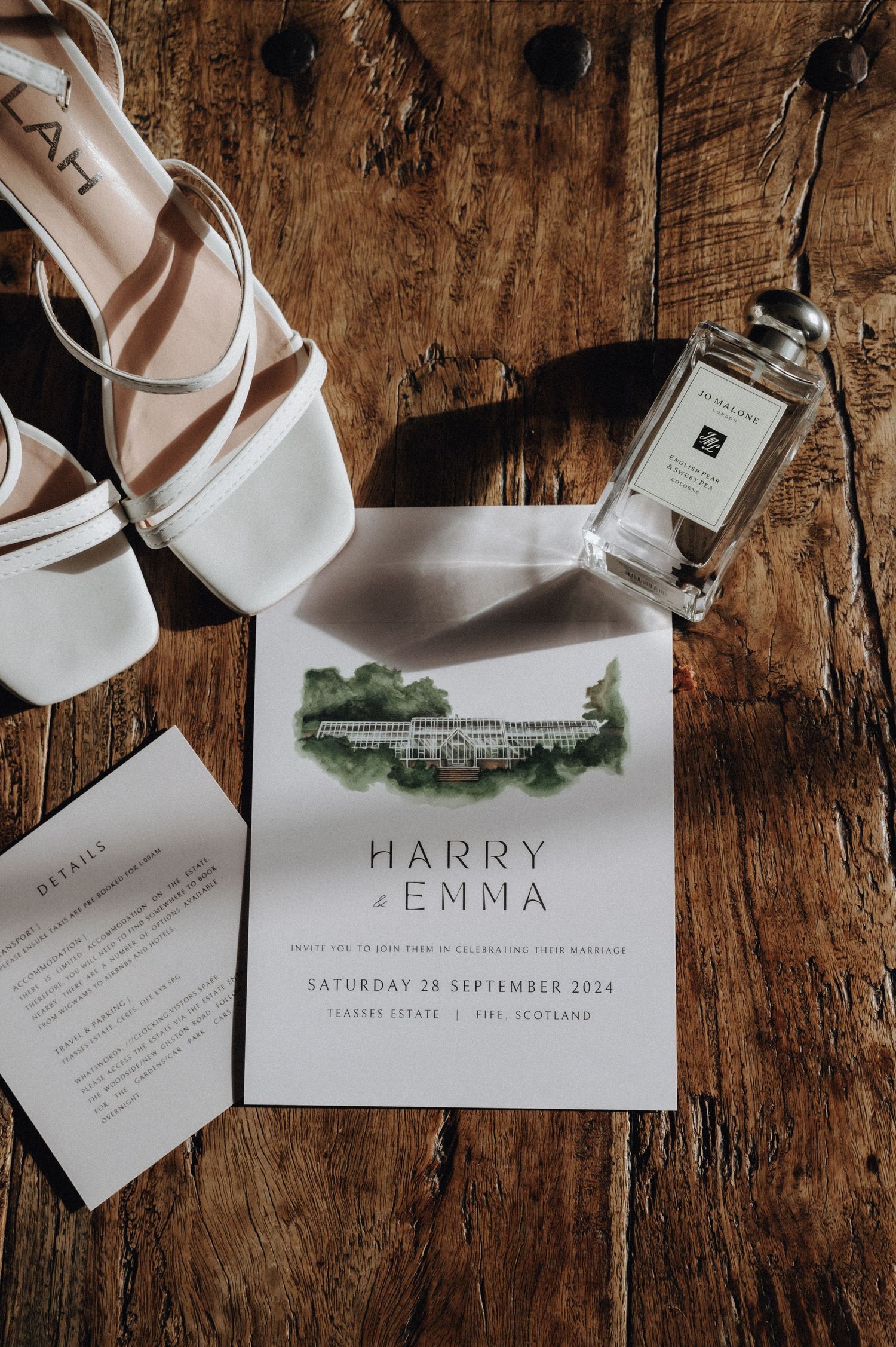 Wedding invitation with venue illustration alongside white shoes and perfume bottle on wooden surface.