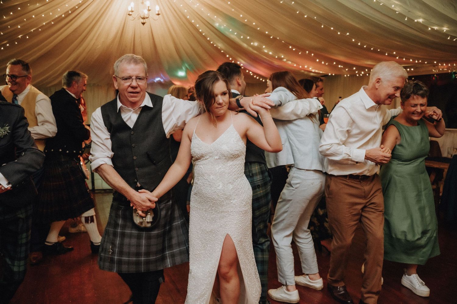Festive wedding reception dance party under draped fabric ceiling with string lights.