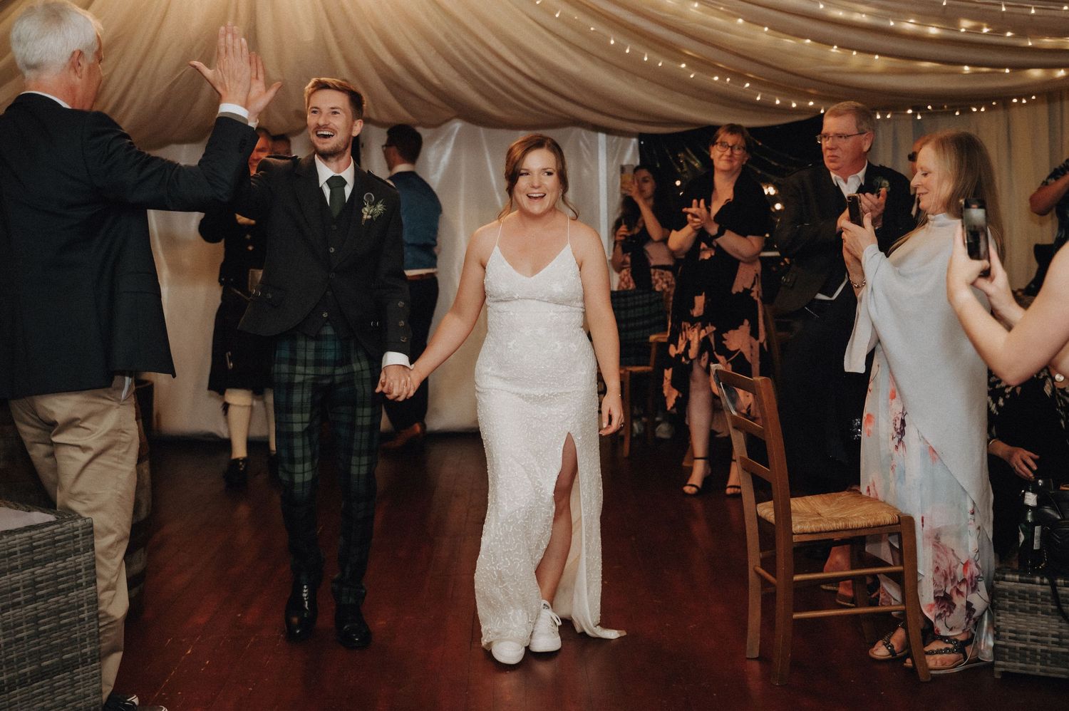 Wedding party entering a beautifully decorated reception tent with white draping and string lights.