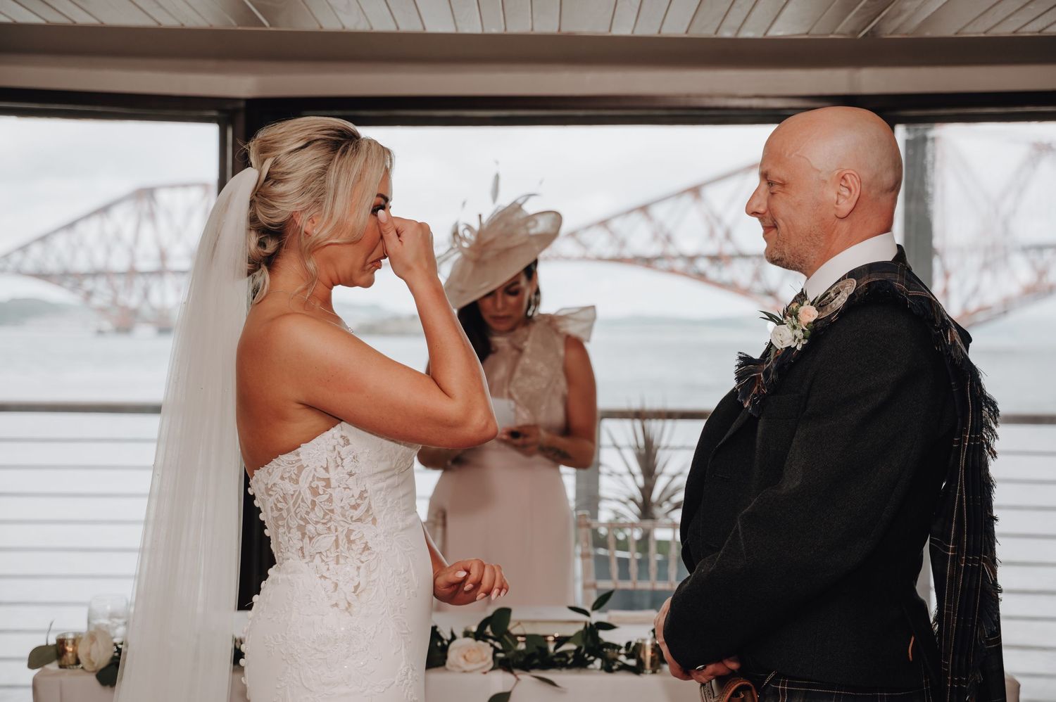 Emotional wedding ceremony moment with bridge visible through window.