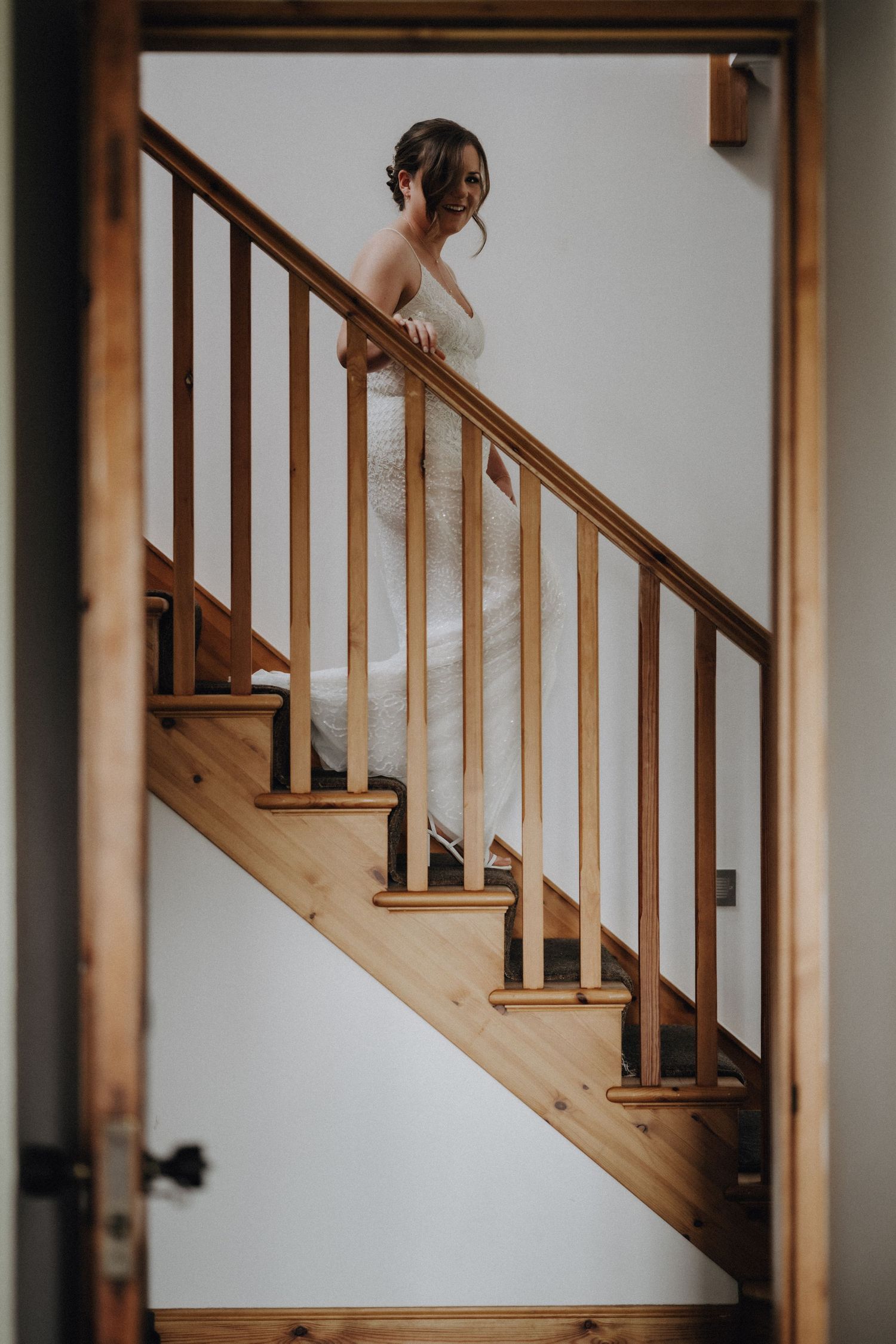 A person in a white wedding dress walking up wooden stairs with a wooden railing.