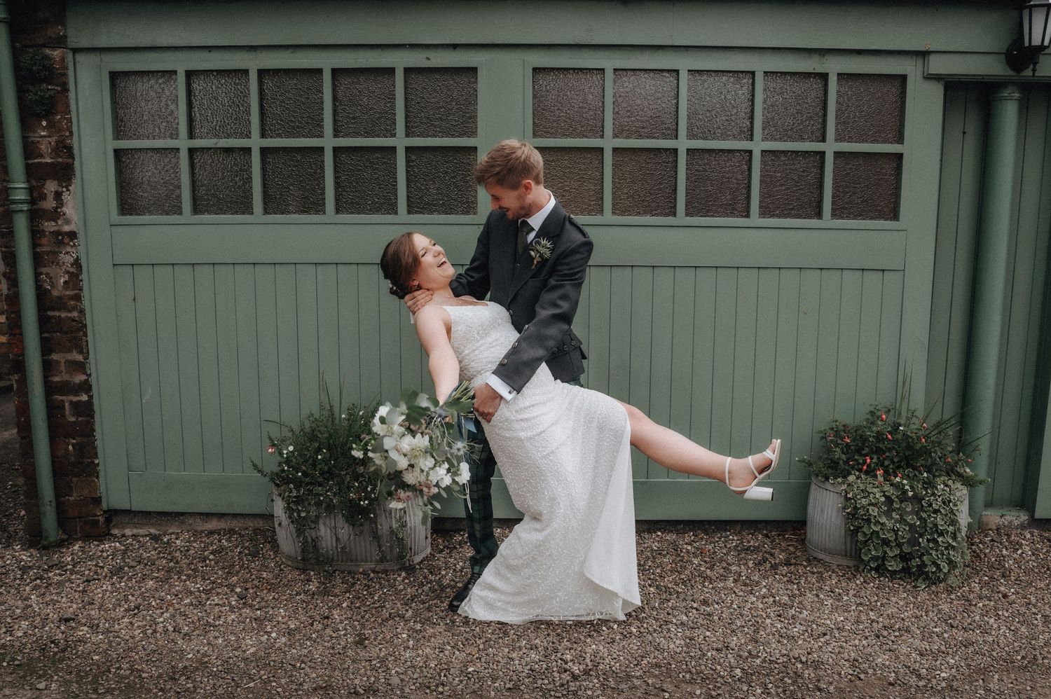 Couple performs romantic dance dip pose in front of vintage green garage door.