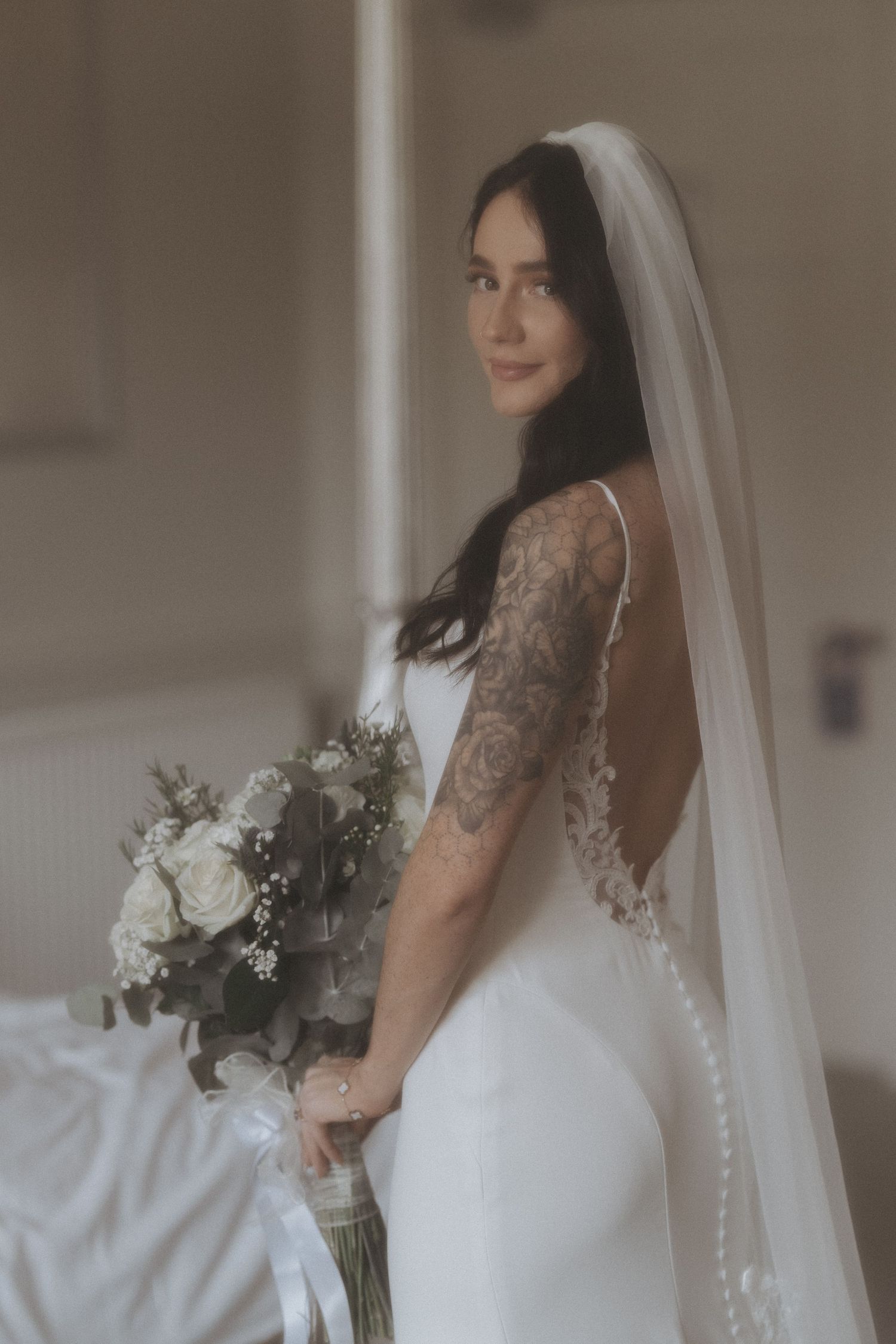 Bride in sleeveless white gown with veil holding white and green bouquet.