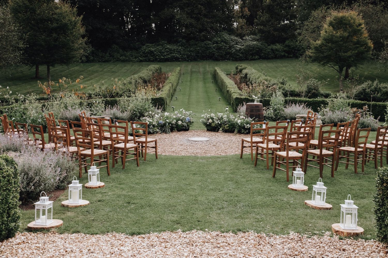 Wooden chairs arranged on a garden lawn for an outdoor wedding ceremony with lantern decorations.