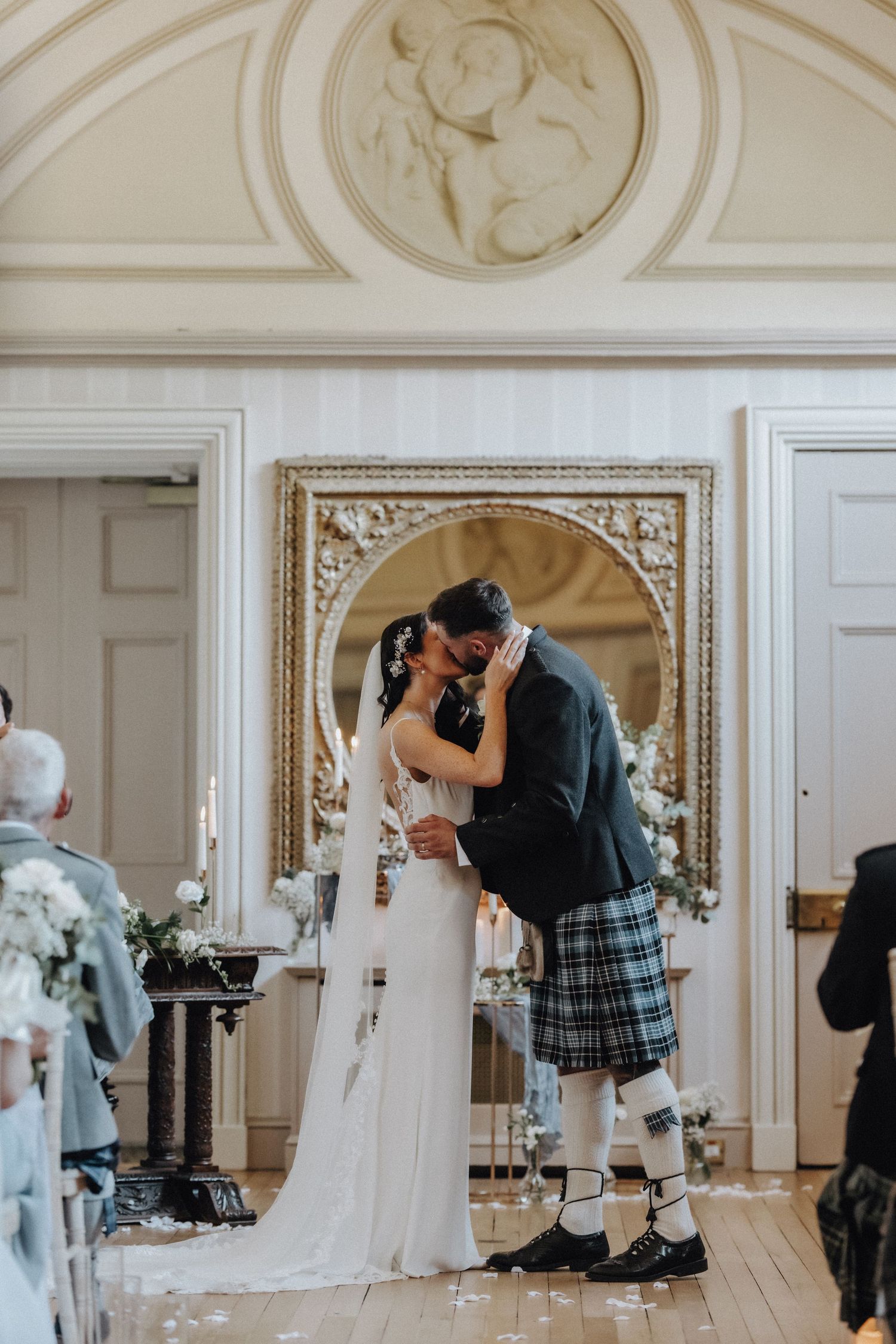Romantic kiss between newlyweds under ornate architectural details with traditional Scottish elements.