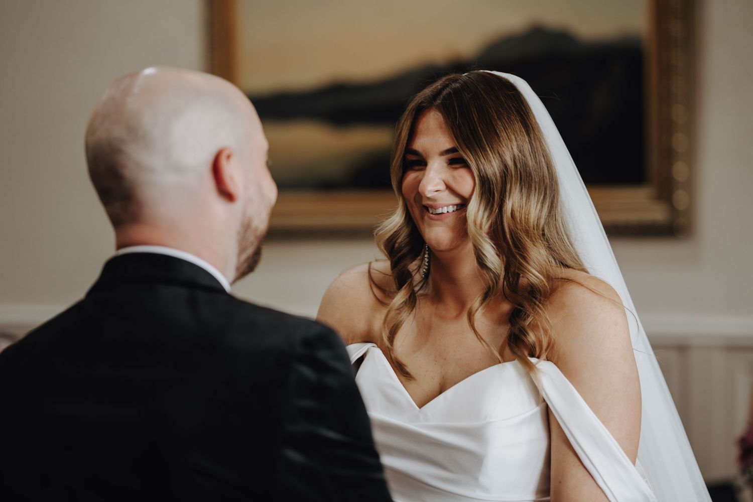 Joyful couple embraces and laughs during wedding celebration in warm indoor setting.