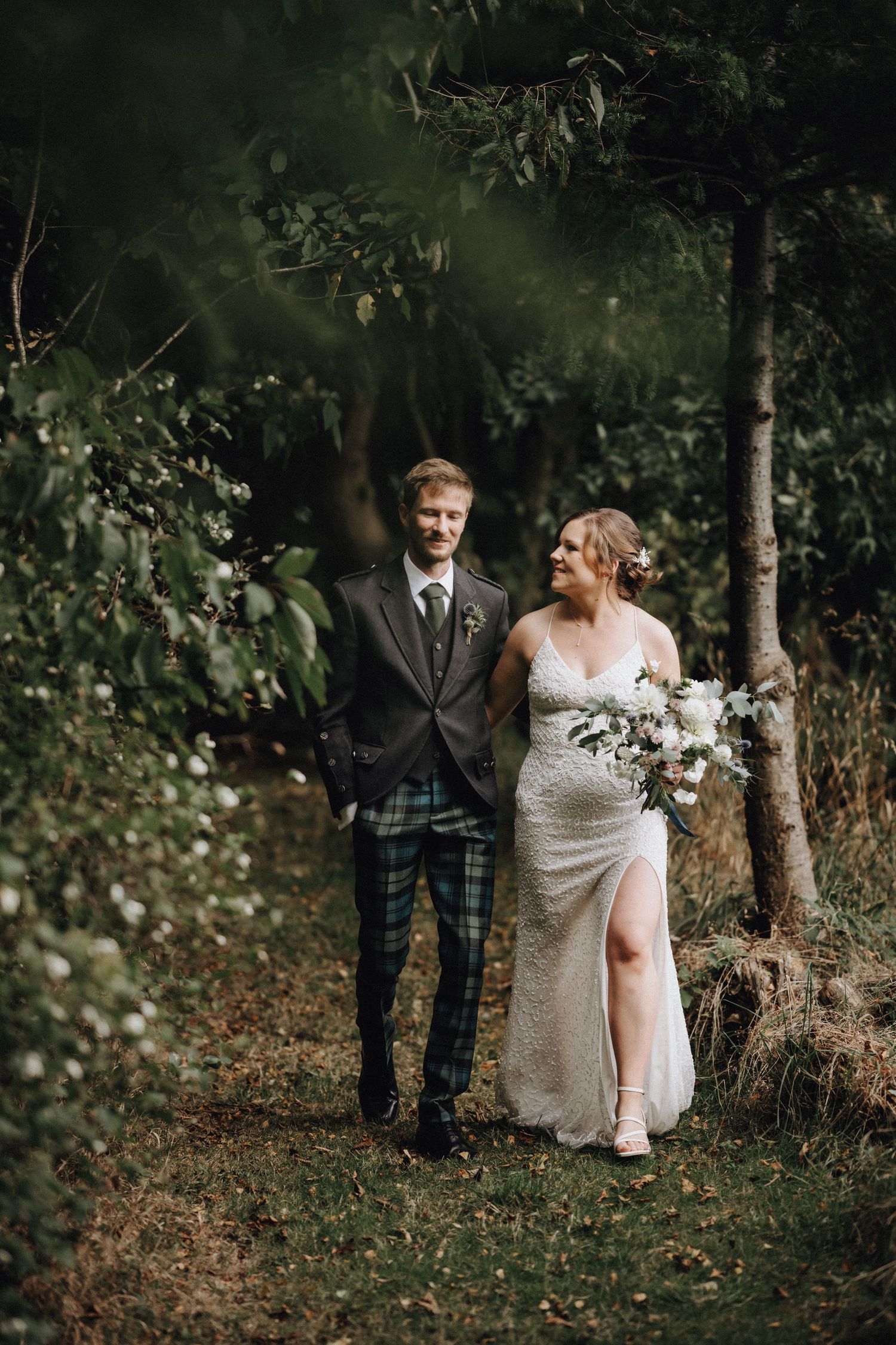 Wedding couple poses in woodland setting with groom in traditional Scottish kilt.