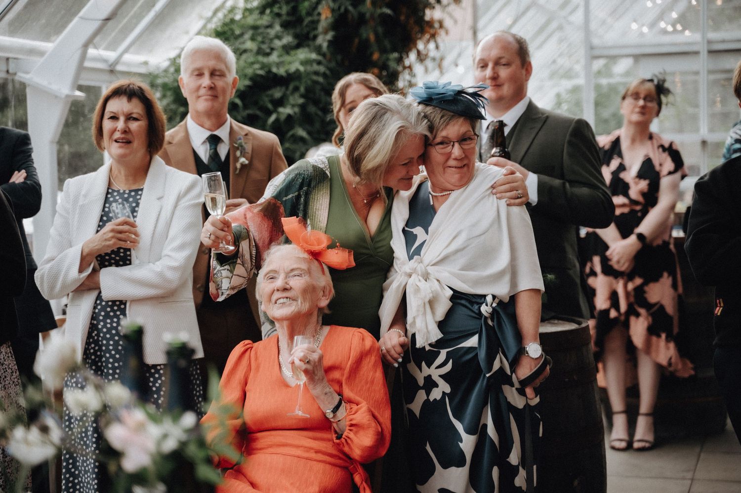Wedding guests enjoying drinks and laughter in a conservatory setting.