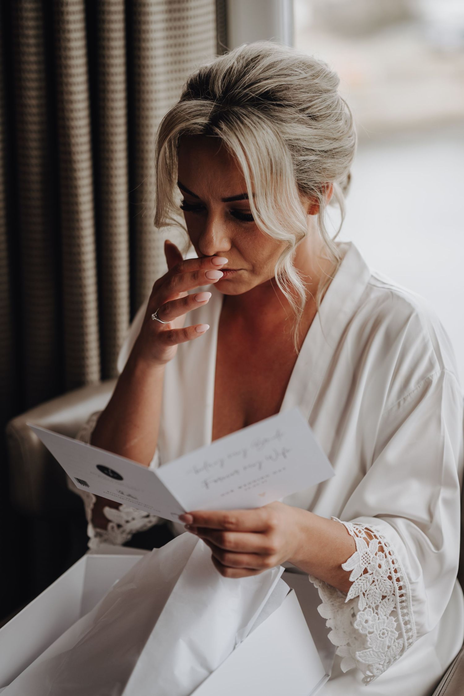 Emotional moment reading letter while wearing white lace robe during wedding preparations.