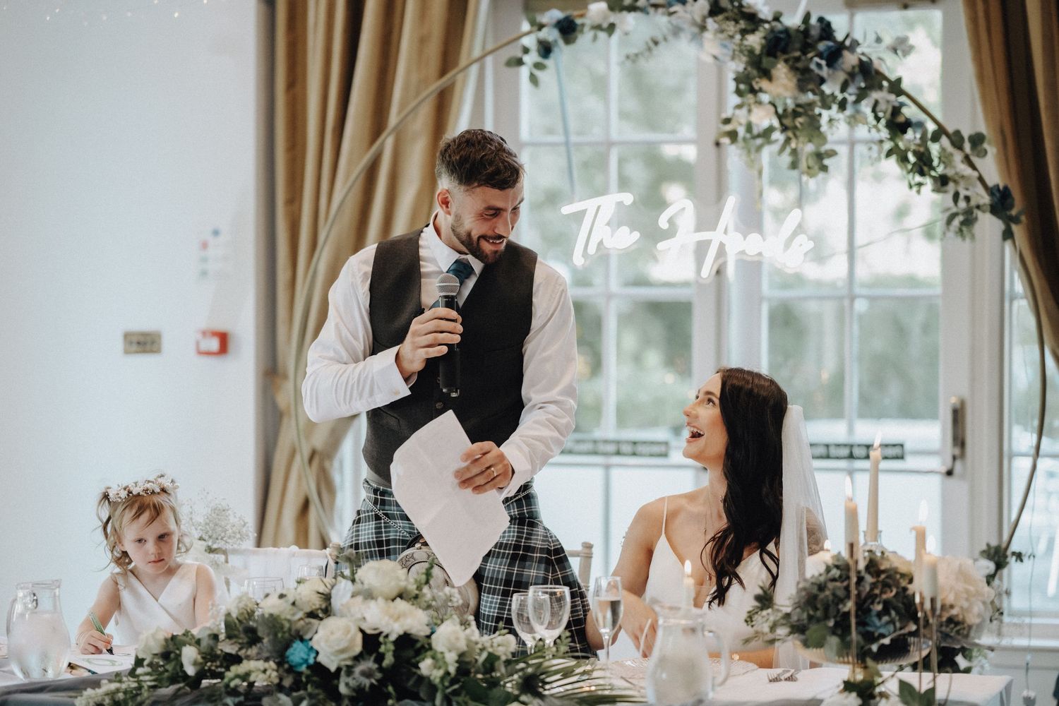 Wedding reception venue decorated with floral arch and draped curtains.