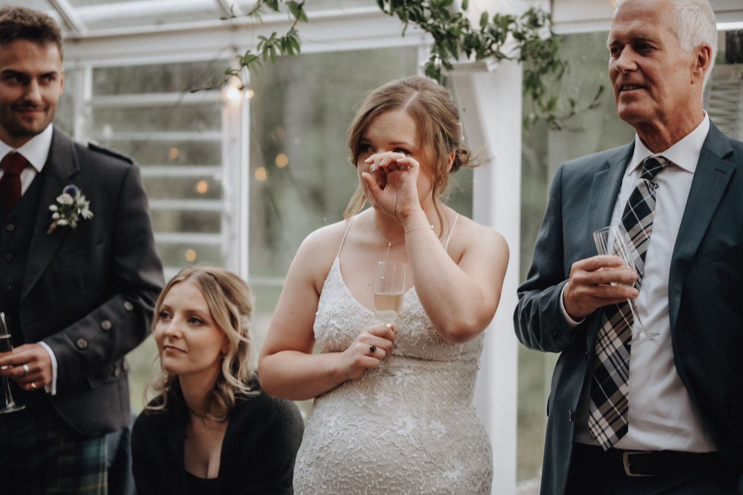 Emotional wedding moment captured in a greenhouse with wedding party looking on.