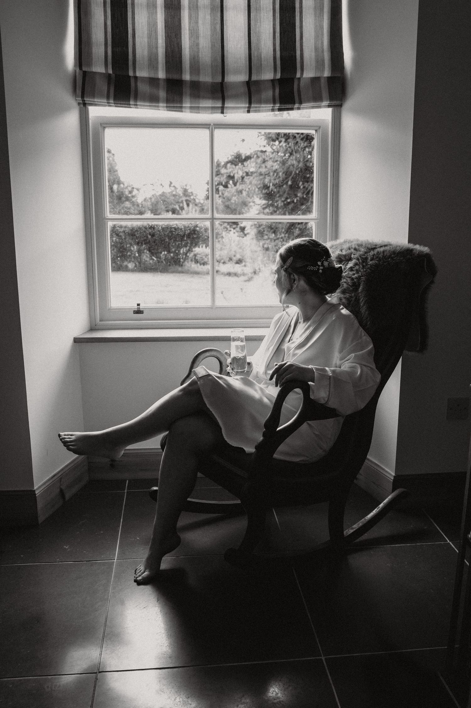 Silhouette of person relaxing in rocking chair by window with roman shade.