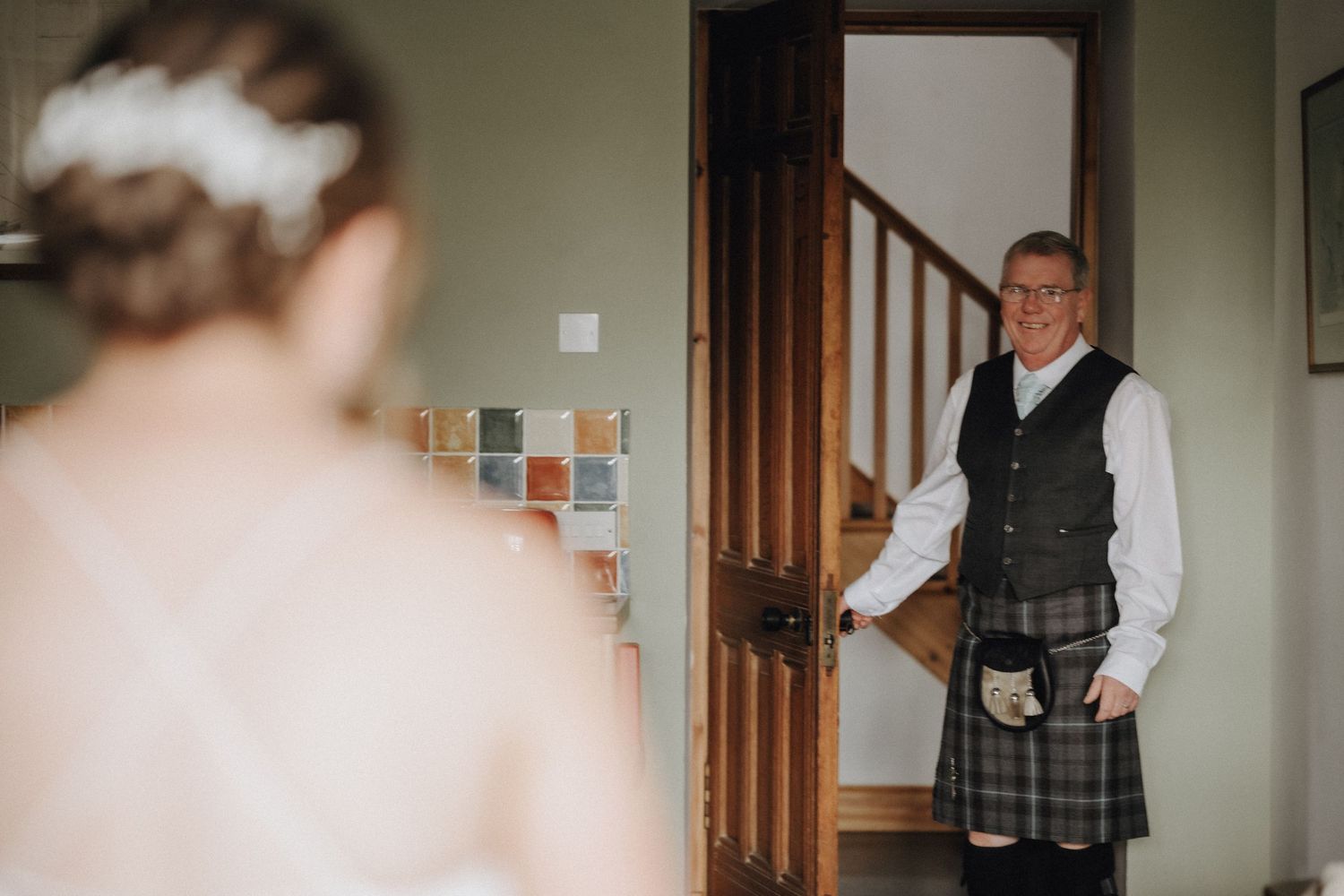 A person wearing traditional Scottish attire stands in a doorway near wooden stairs.