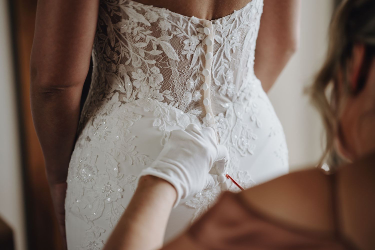 Close-up of intricate lace details on back of wedding dress being fastened.