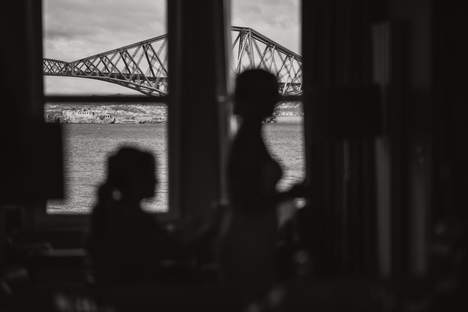 Silhouettes of figures seen through window with iconic bridge structure visible in background.