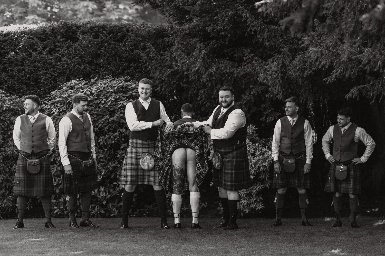 A vintage black and white photo of men in traditional Scottish kilts posing outdoors.