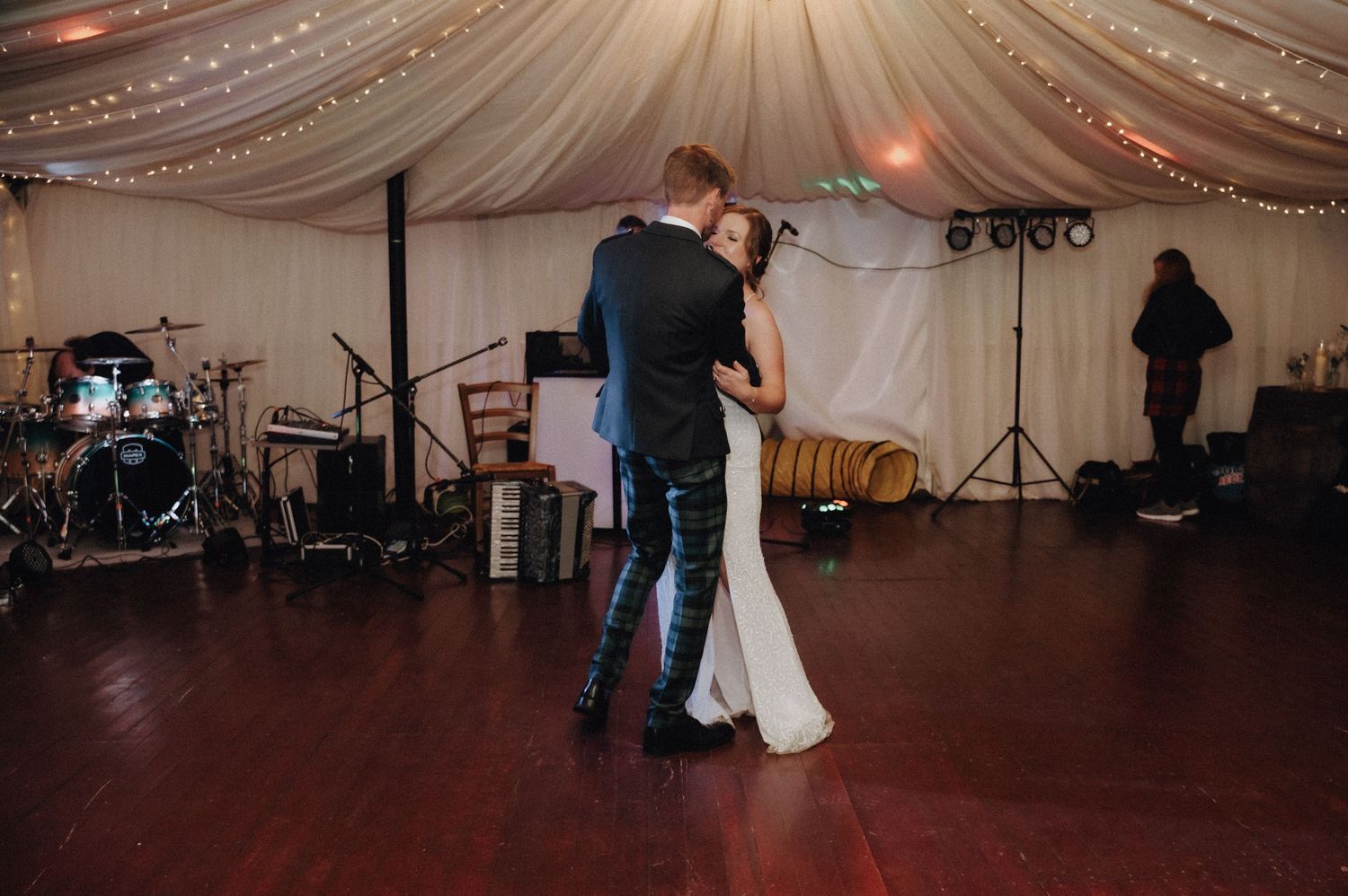 A couple shares their first dance in an elegant tent venue with fairy lights and band equipment.