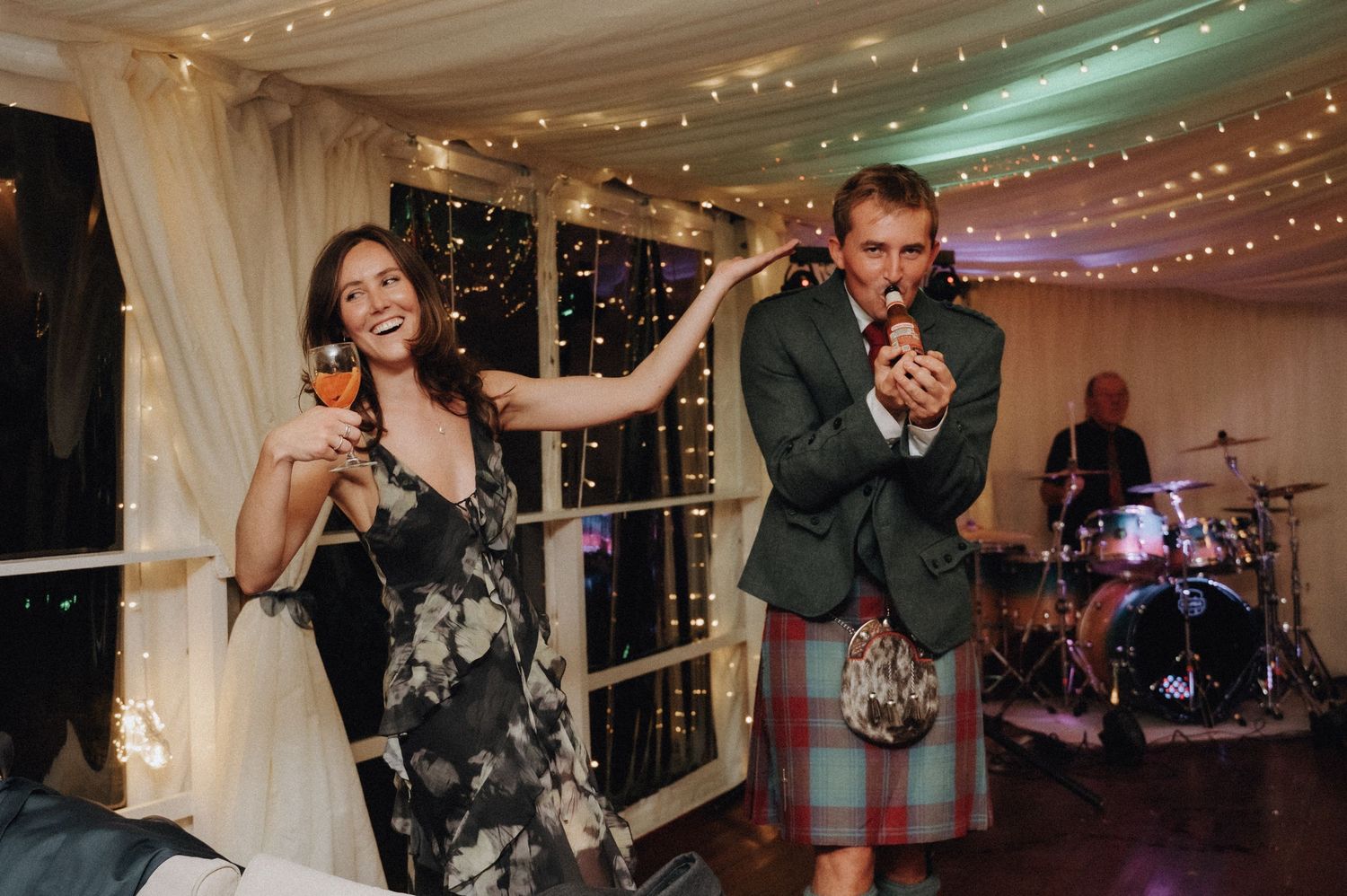 Wedding guests having fun and dancing in traditional Scottish attire at reception.