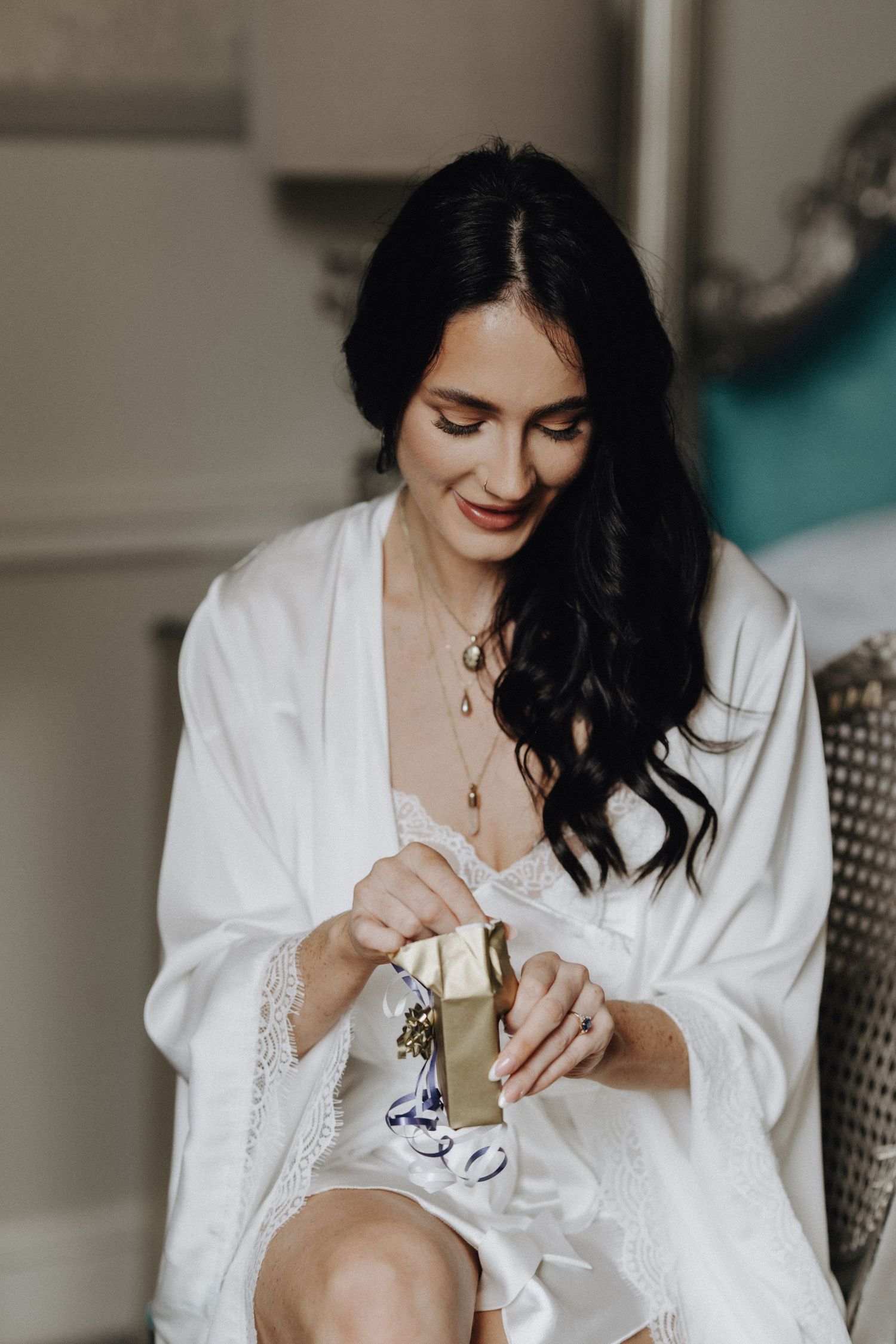 Woman in white robe smiling while holding champagne during wedding morning preparations.