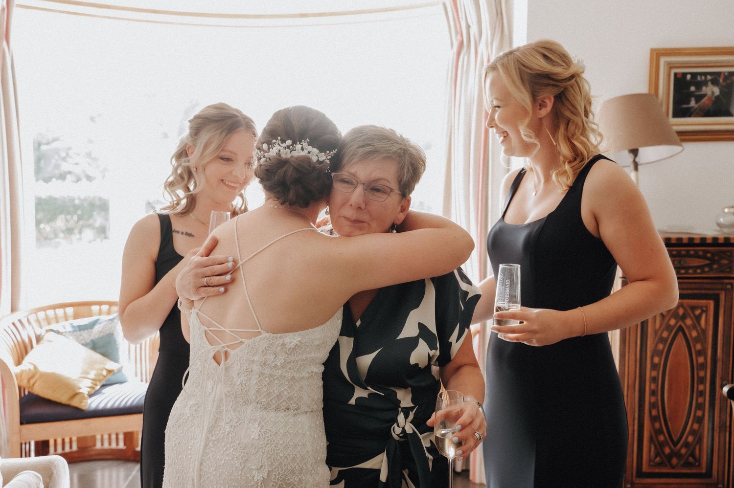 Emotional group hug during wedding preparations in sunlit room.