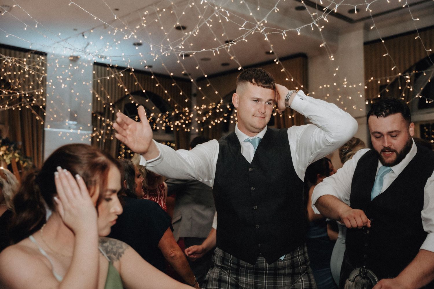 Wedding guests dancing energetically in kilts at Scottish reception celebration.