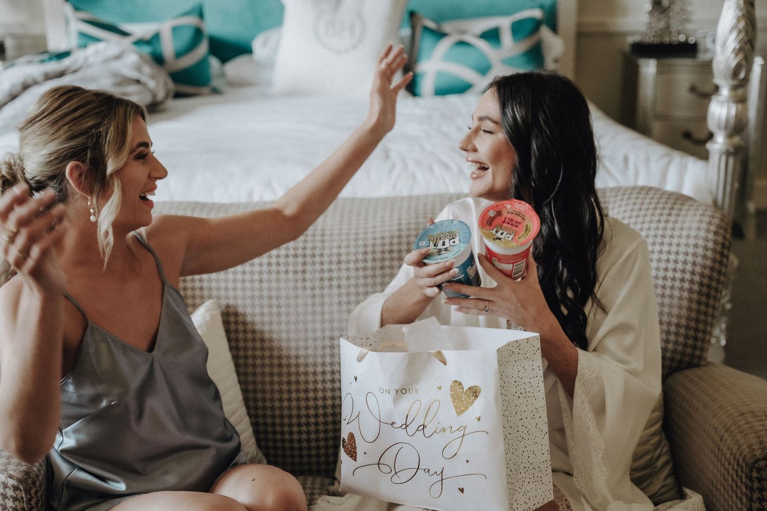 Two people sharing joyful laughter while sitting on a couch with gift bags and cocktails.