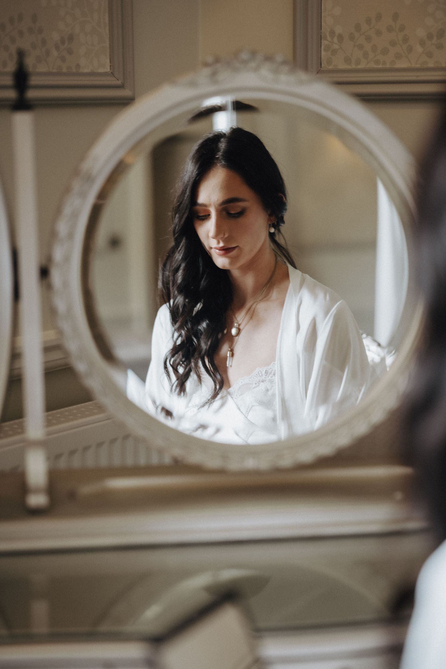 A reflection in a round mirror shows a woman with dark hair wearing white bridal attire.