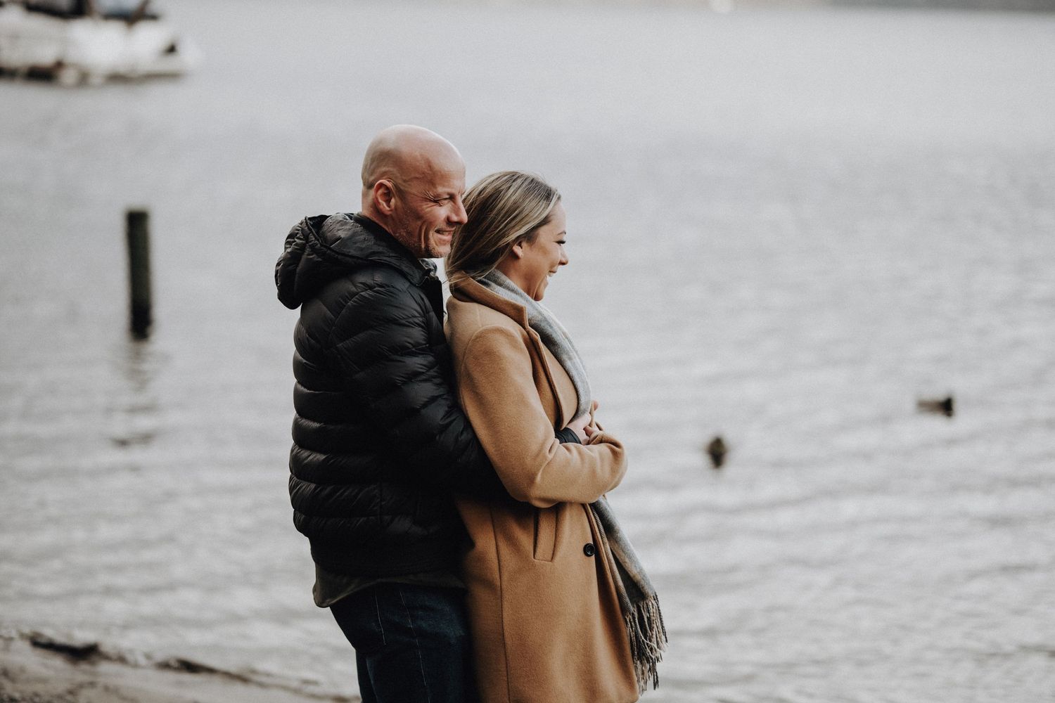 A couple embraces while enjoying a peaceful moment by a lake with mountain views.