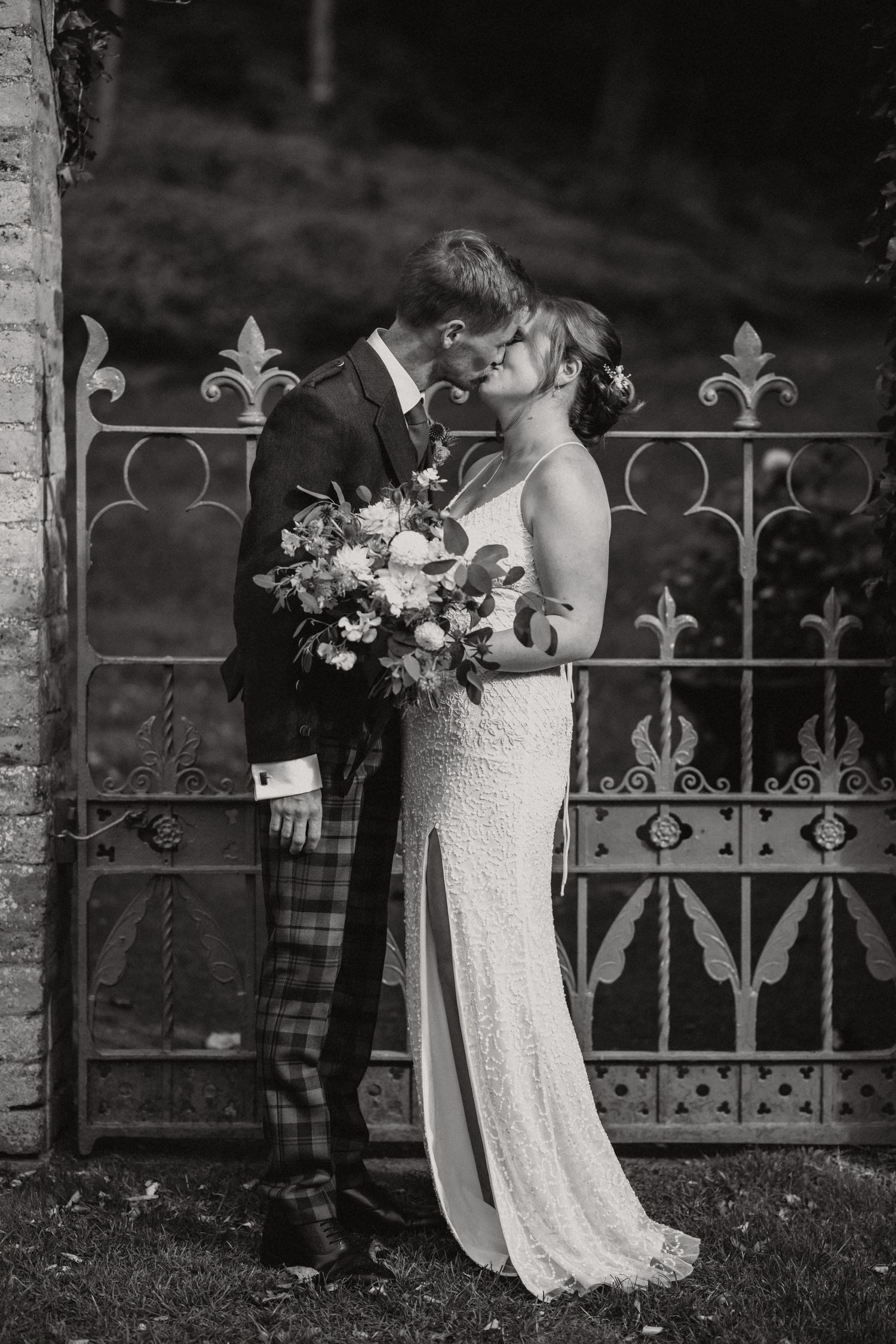 Romantic black and white photo of newlyweds sharing a moment by decorative iron gates.